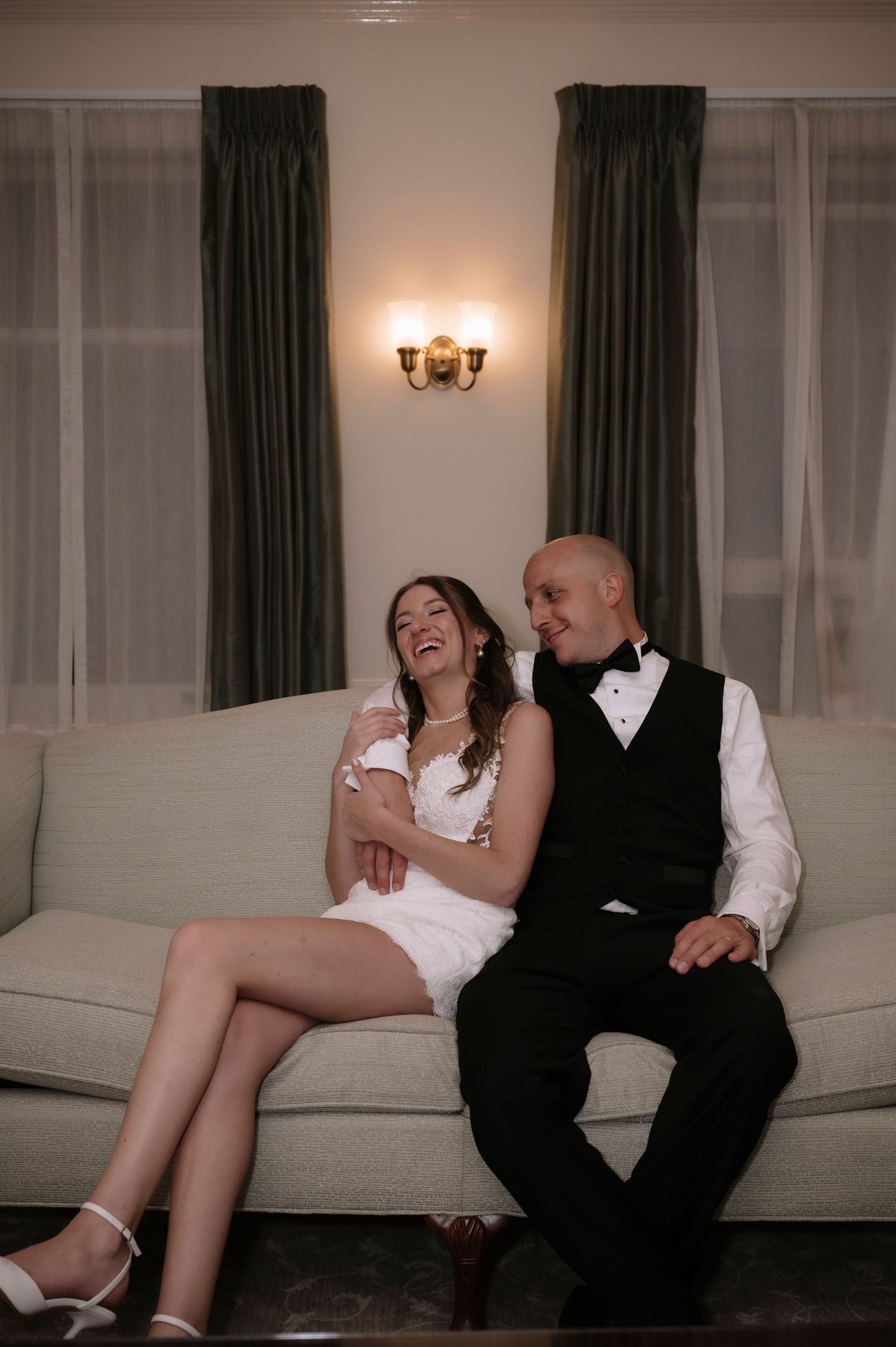 A couple sitting on a sofa share a joyful moment together during their wedding reception celebration.