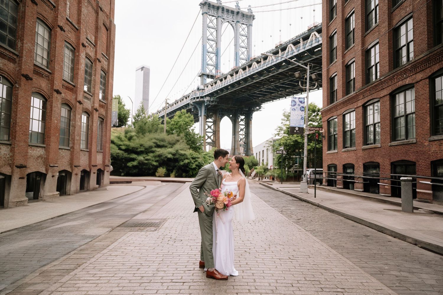 A romantic wedding photo in front of the Manhattan Bridge in DUMBO Brooklyn on a quiet cobblestone street.