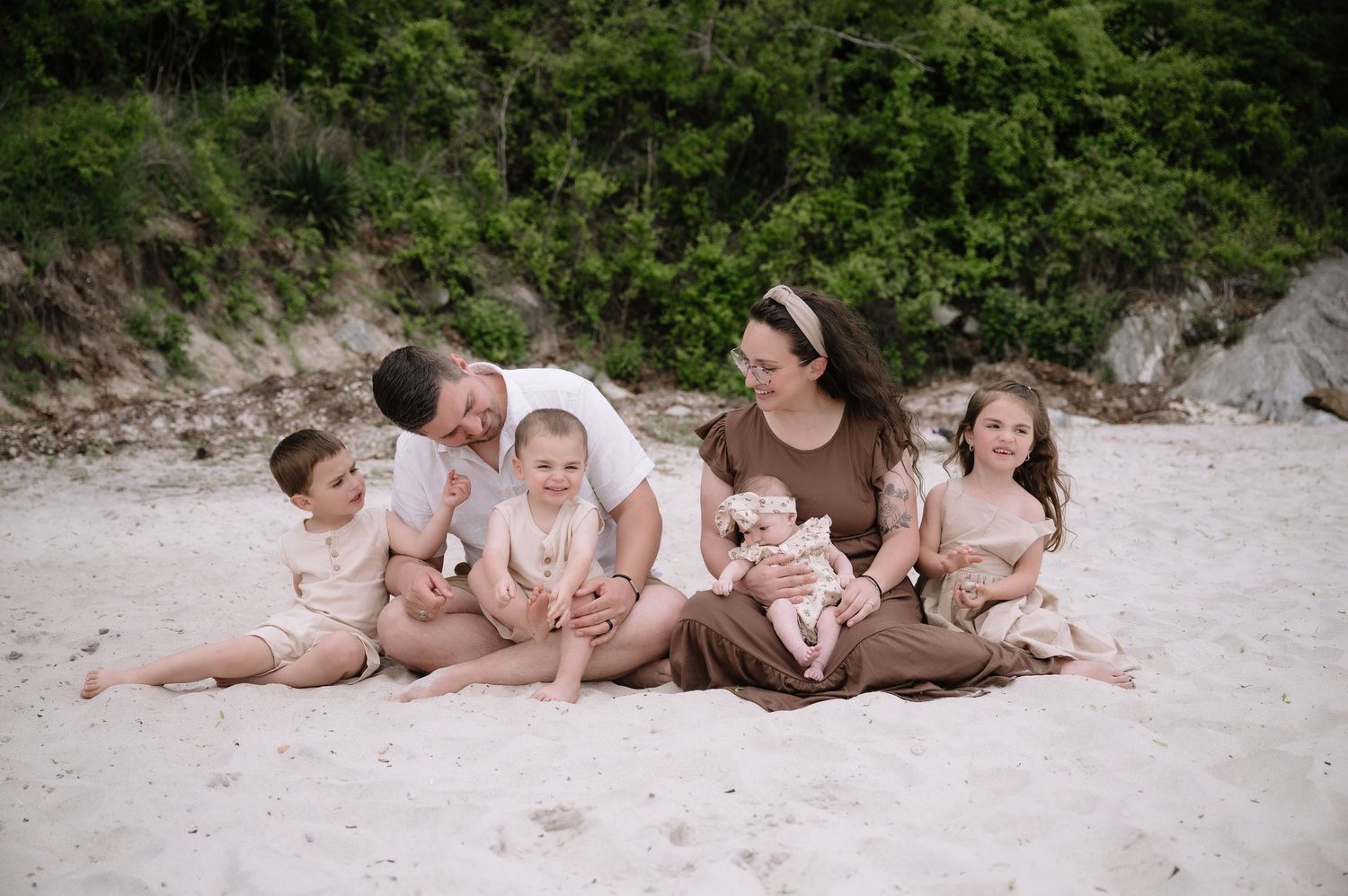 Family sitting together on a sandy beach with natural cliffs and greenery in the background.