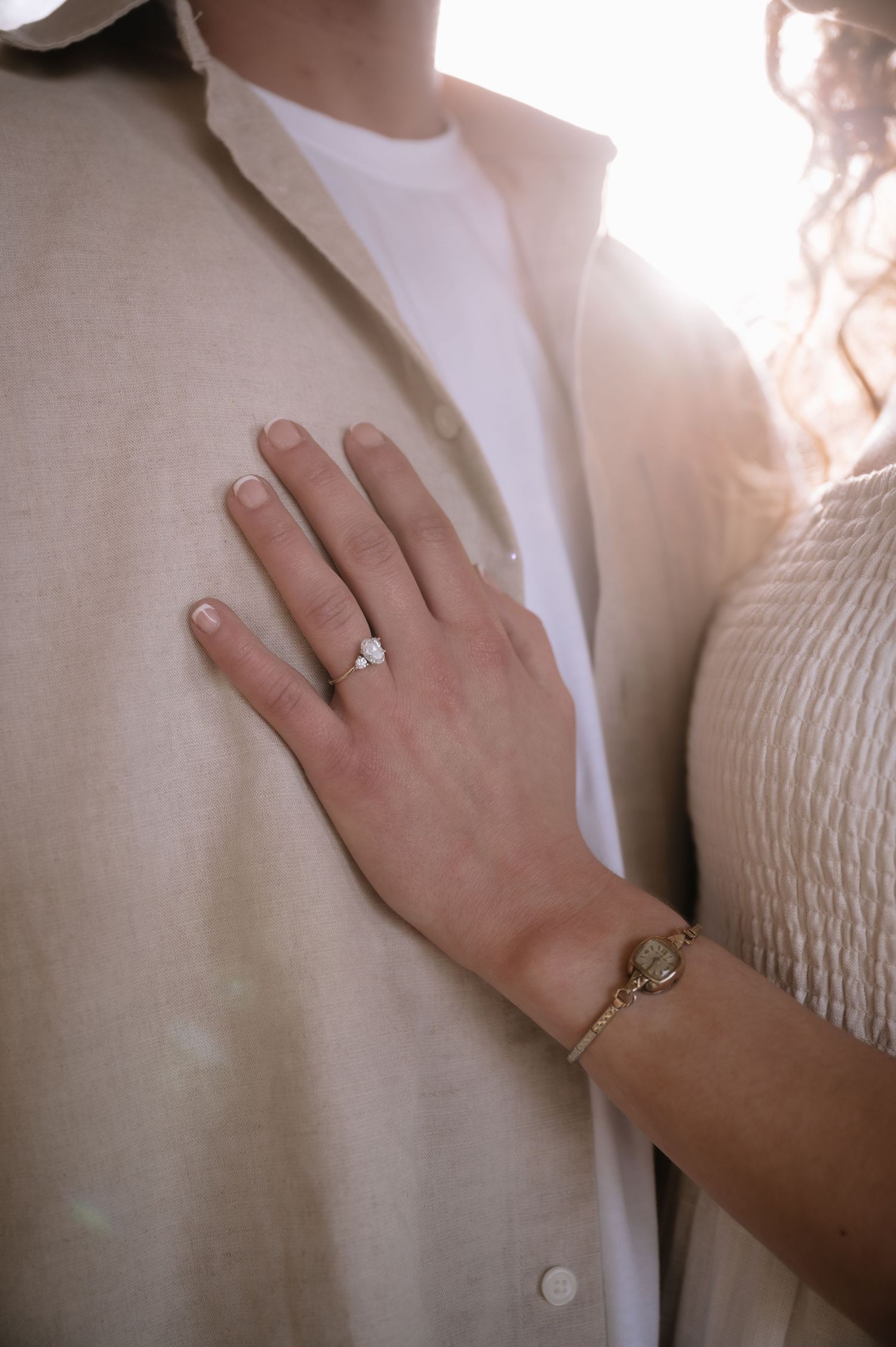 A close-up shot of an engagement ring and bracelet against light clothing.