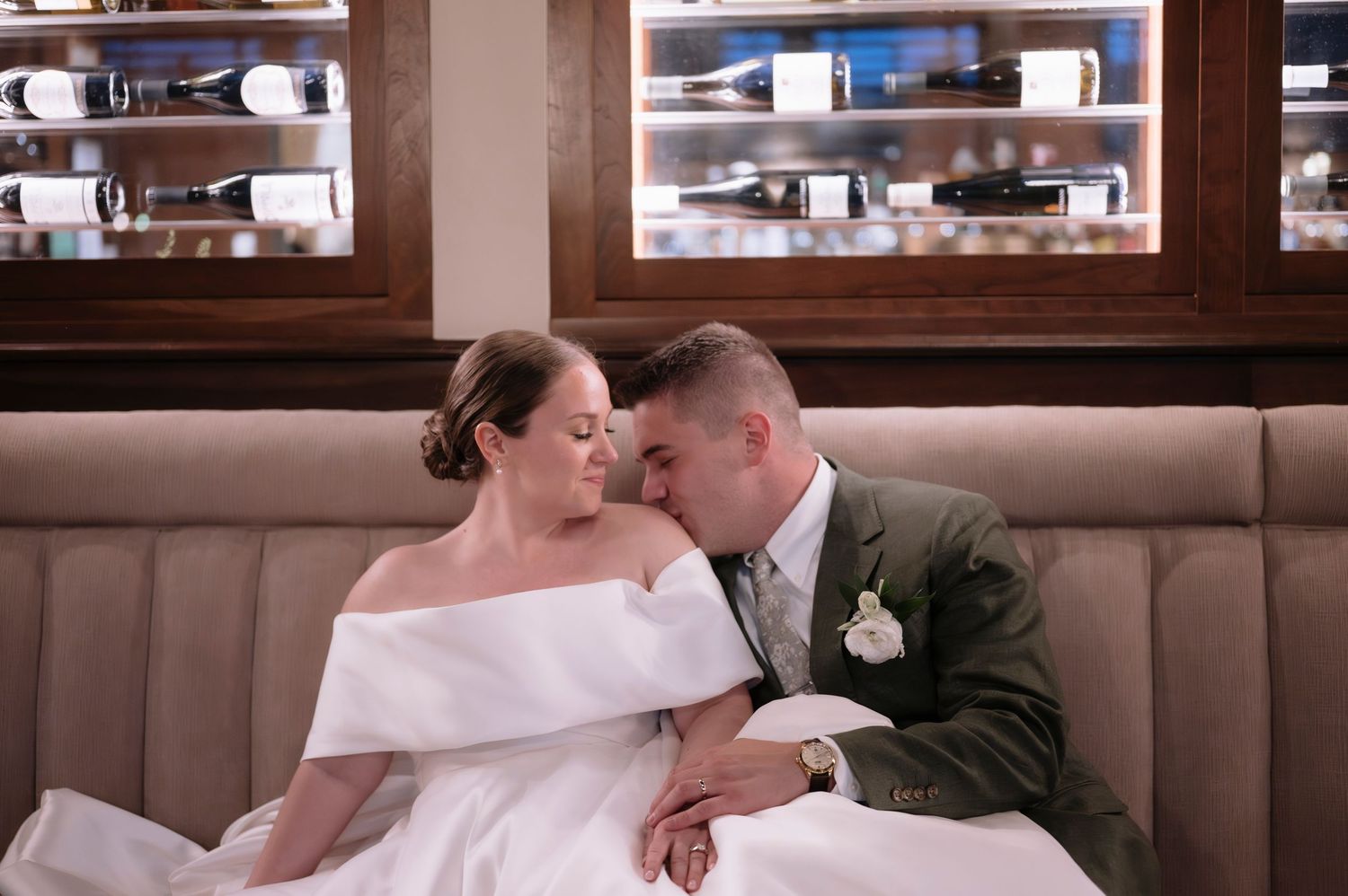 Bride and groom share a romantic moment seated in a cozy restaurant booth on their wedding day.