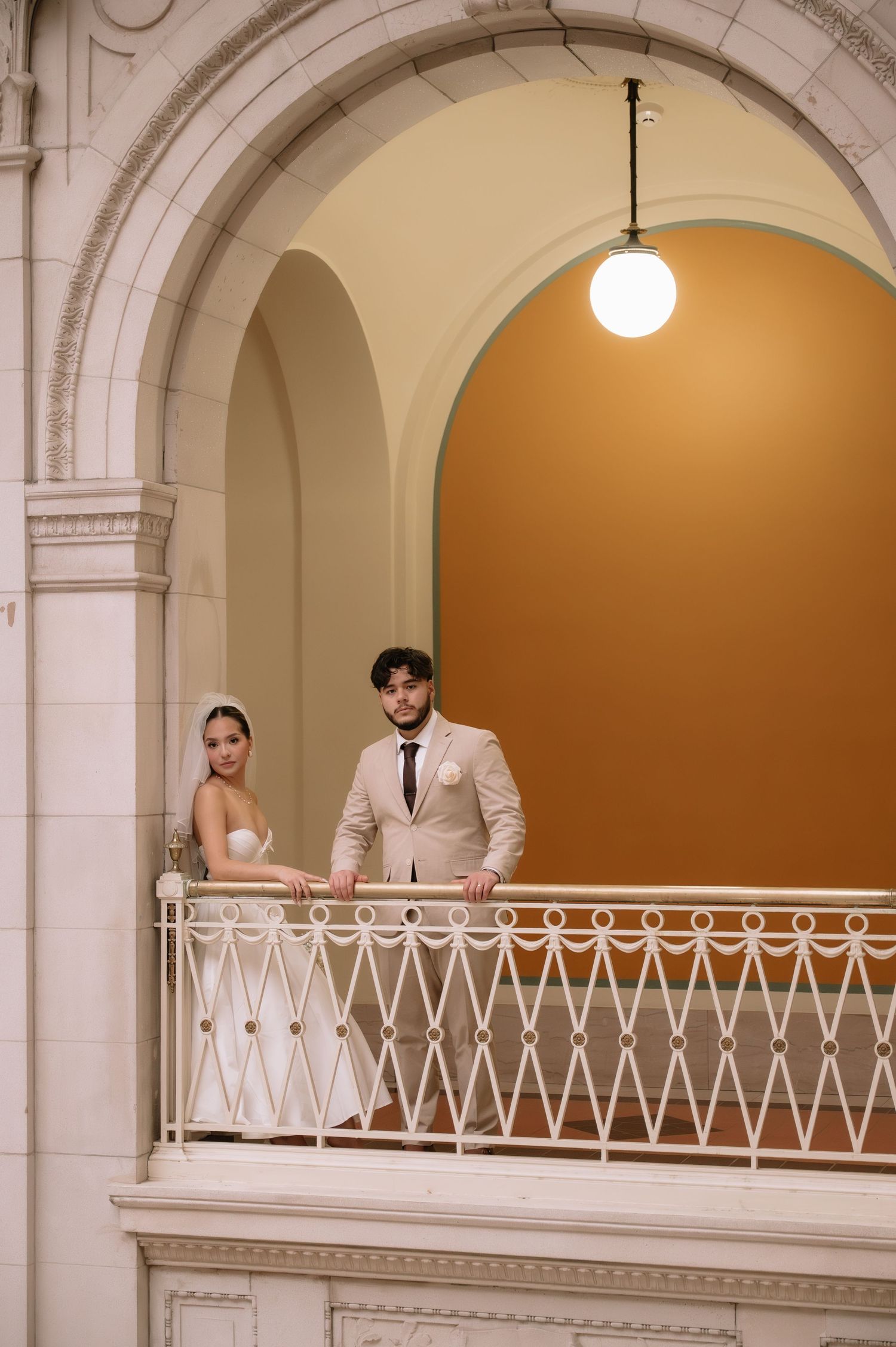 Wedding couple stands together on an elegant white balcony with classical architectural features.