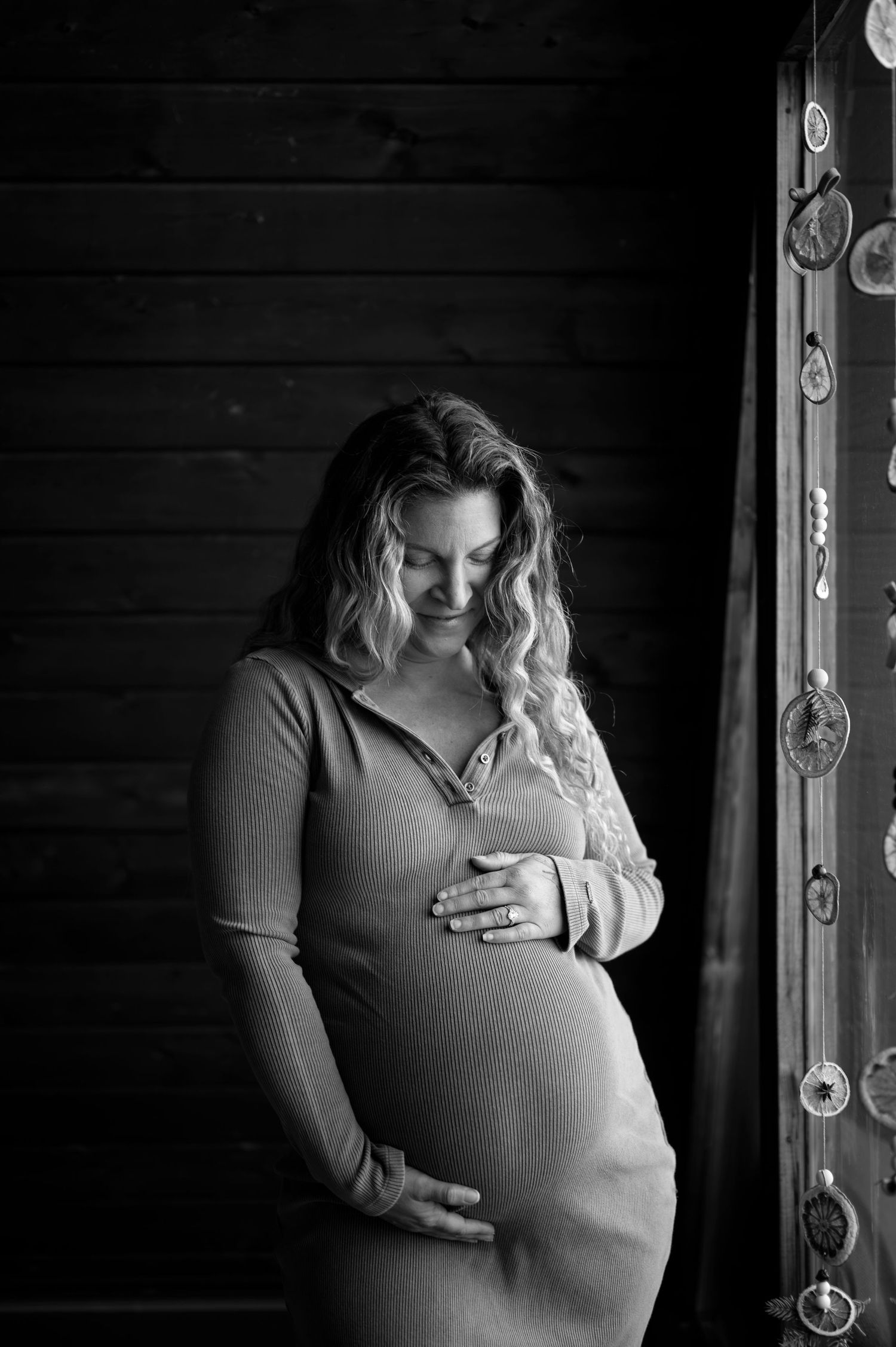 Black and white maternity photo series showing gentle moments and belly silhouettes against dark wooden backdrop.