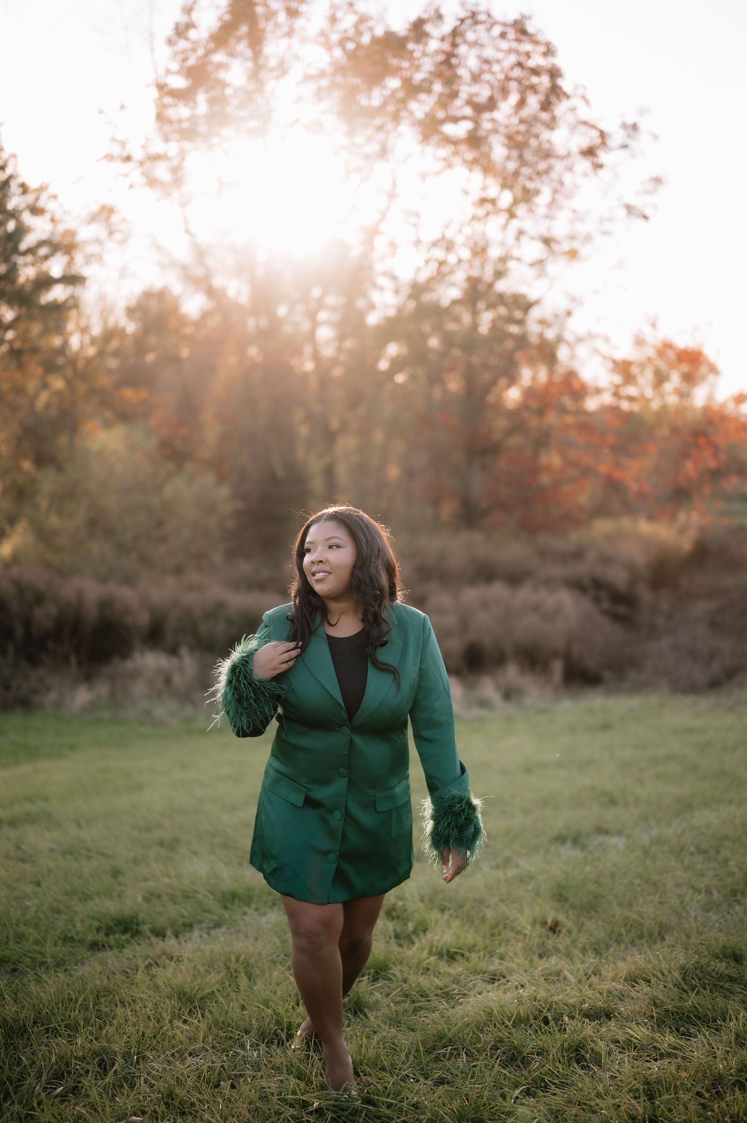 A person in an emerald green blazer poses playfully in a sunlit meadow during golden hour.