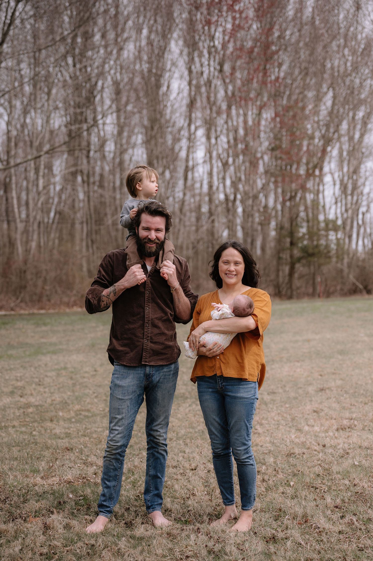 A family stands barefoot in a grassy field during autumn.