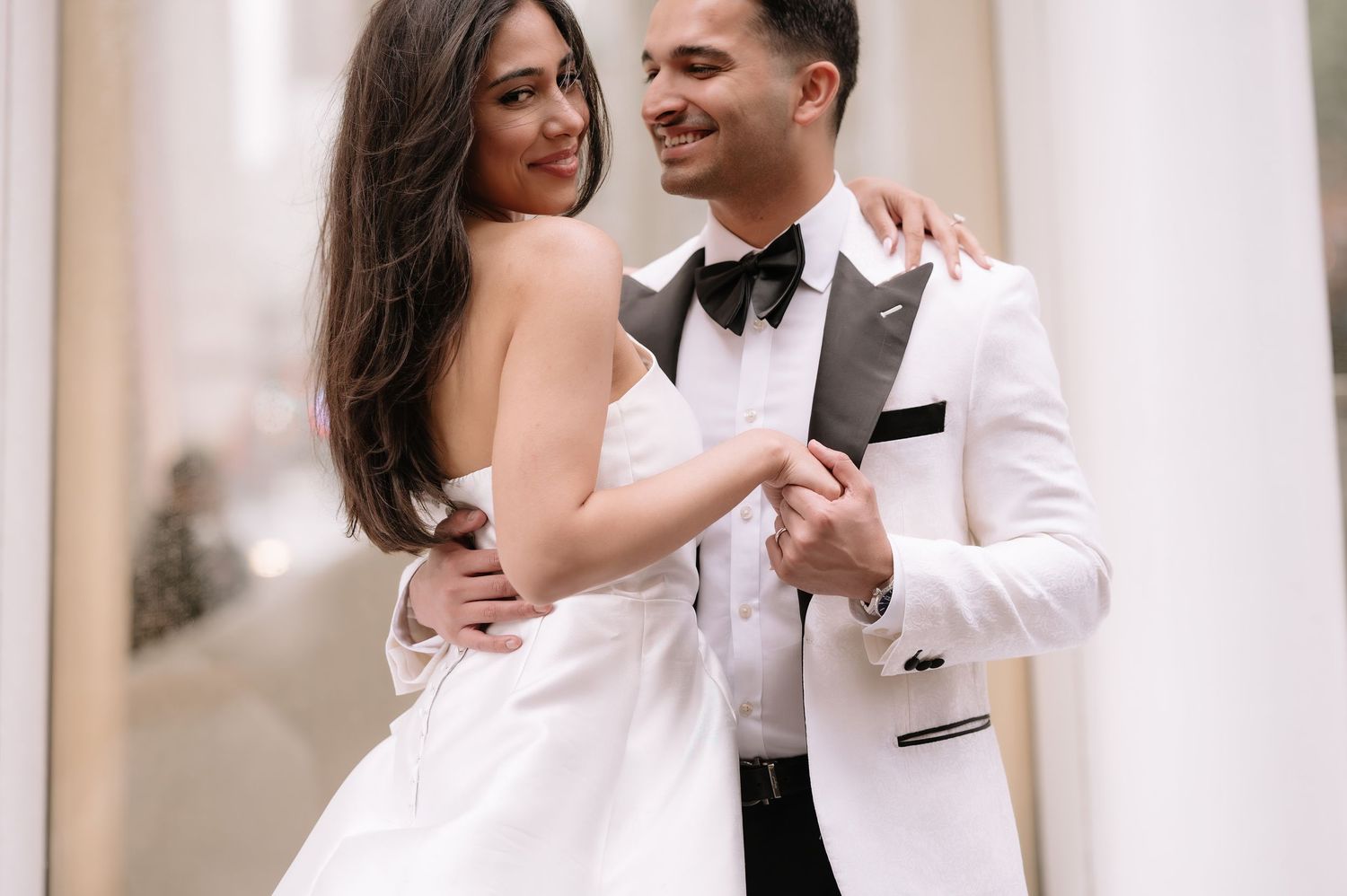 Close-up of couple in formal wear sharing tender moment against light architectural background.