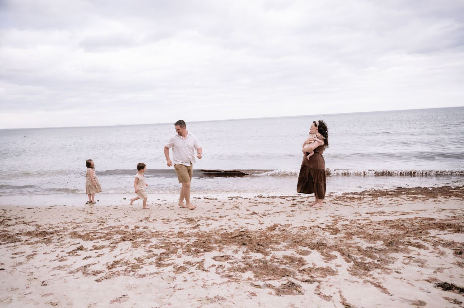 Family enjoying a beach day with children playing in the sand while waves crash on the shore under cloudy skies.