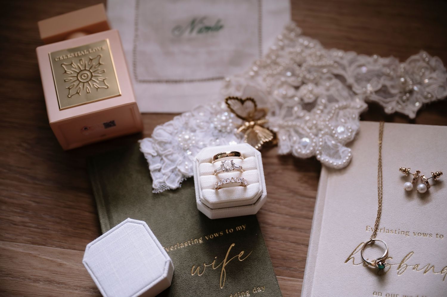 Elegant wedding flat lay with diamond rings in velvet box, gold jewelry, lace details, and sentimental cards.