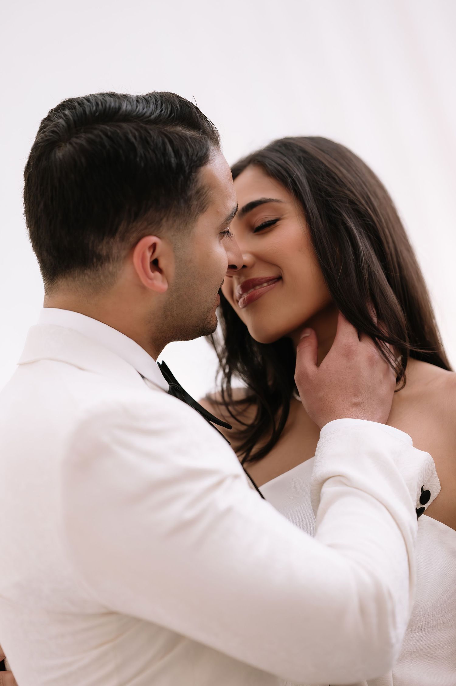 An intimate close-up portrait of a couple in formal white attire.