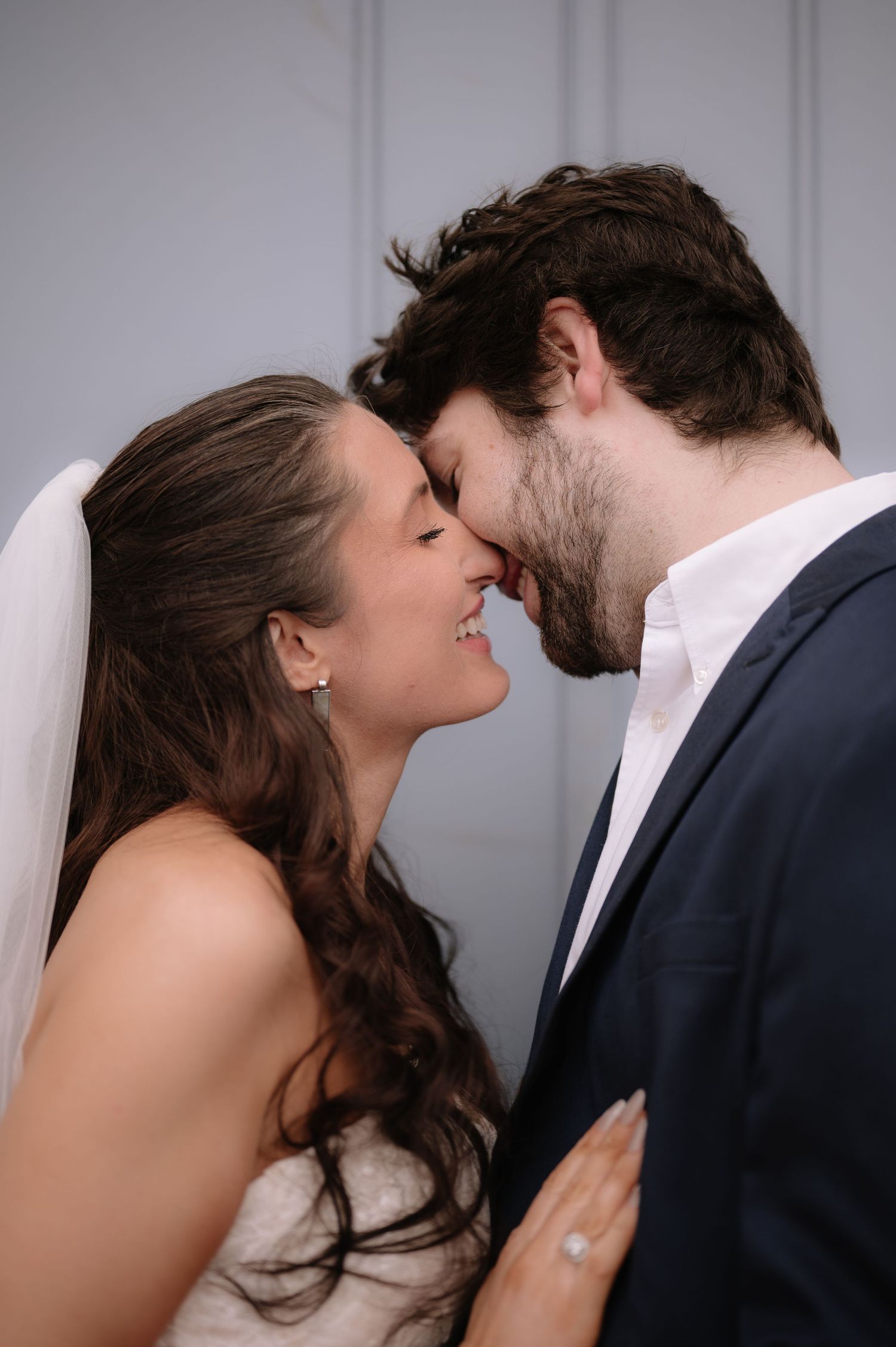 Wedding couple sharing an intimate close-up moment against a white wall.