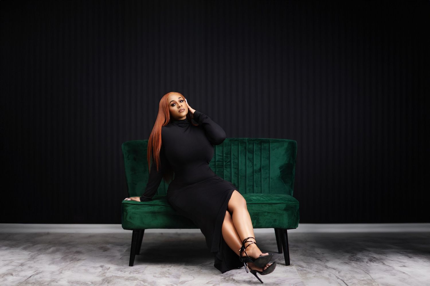 Glamorous portrait on emerald velvet couch wearing black dress with high slit.