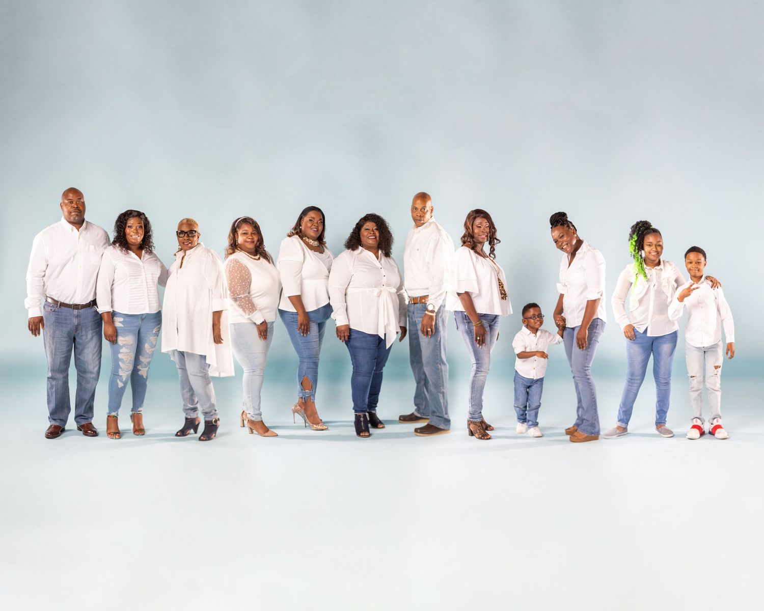Large family portrait in coordinated white and denim outfits against light background.