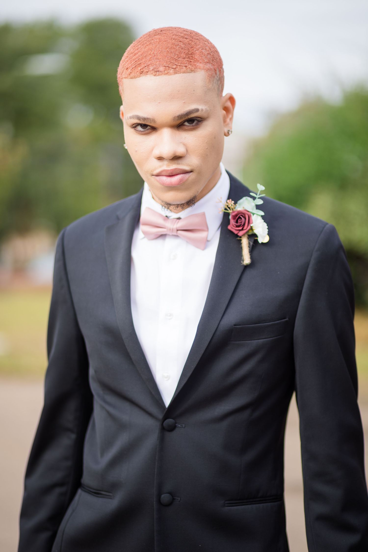 Formal portrait of person in black tuxedo with pink bow tie and rose boutonniere.