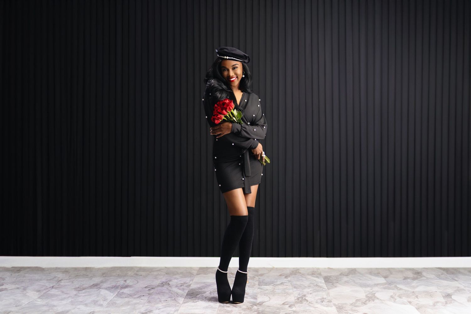Fashion portrait with roses showing winter style with boots and hat against dark background.