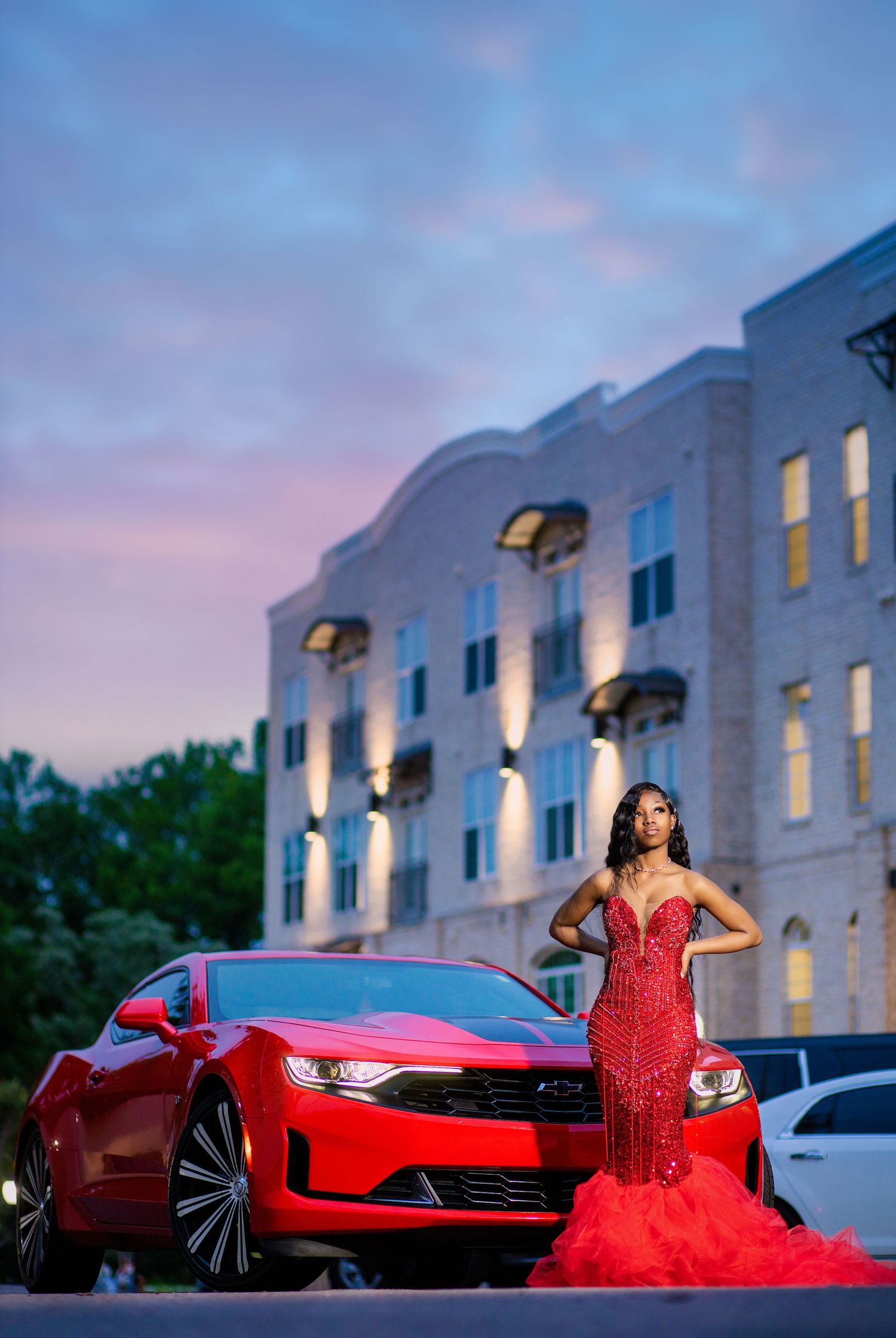 A glamorous evening photoshoot featuring a red mermaid dress and matching red sports car.