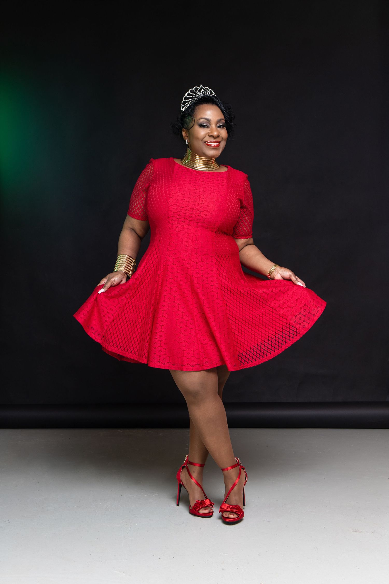 Woman in red polka dot dress and matching heels twirls against dark studio background.
