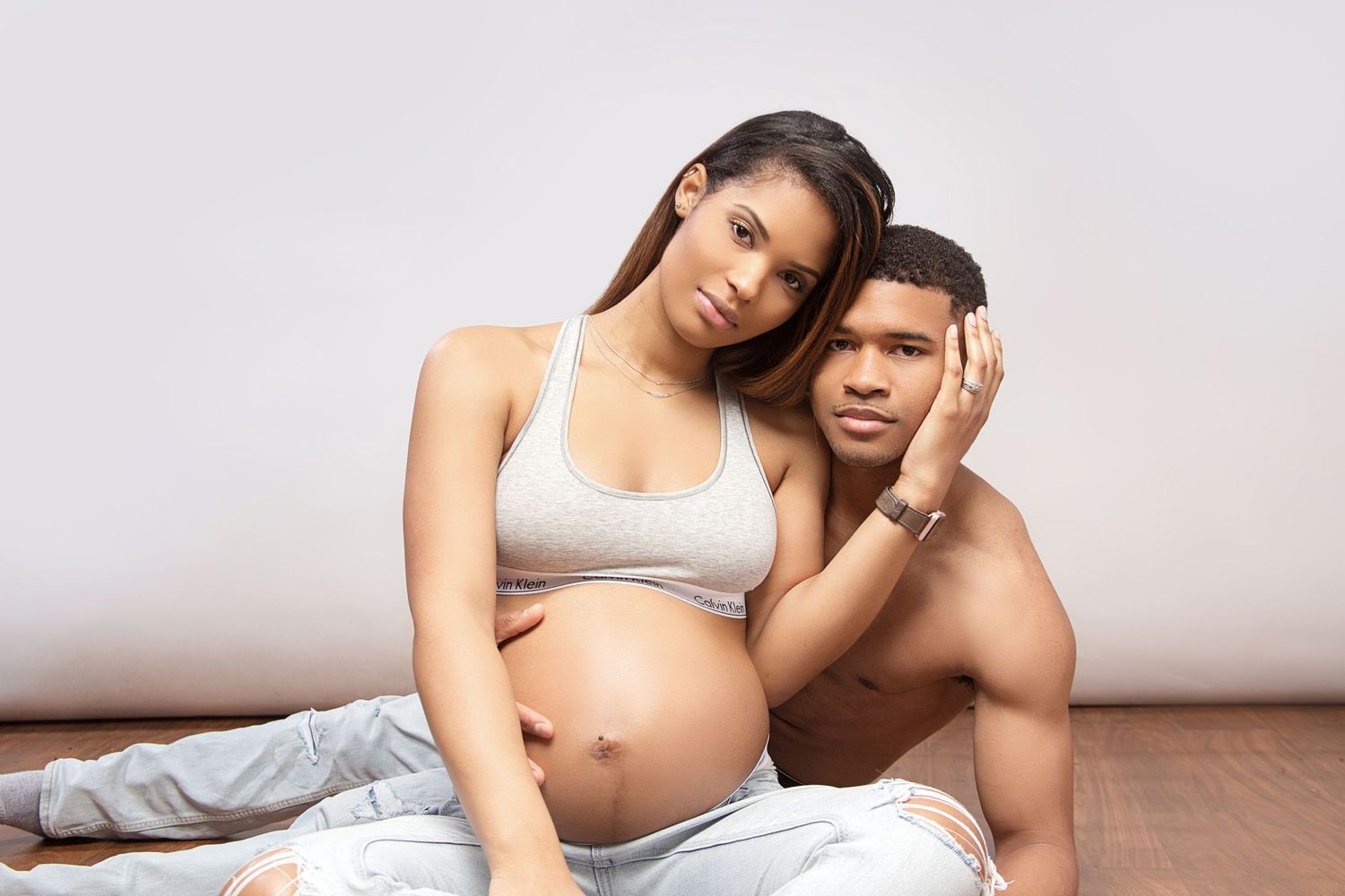 Intimate photo of an expecting couple lounging together on hardwood floor in casual attire.
