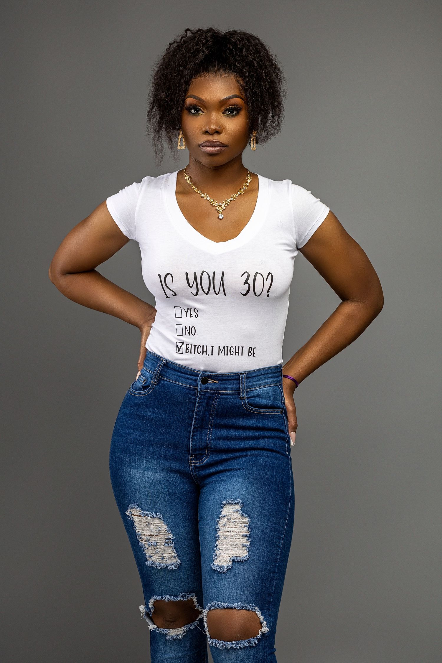 Portrait of woman in casual attire with ripped jeans and graphic t-shirt against gray background.