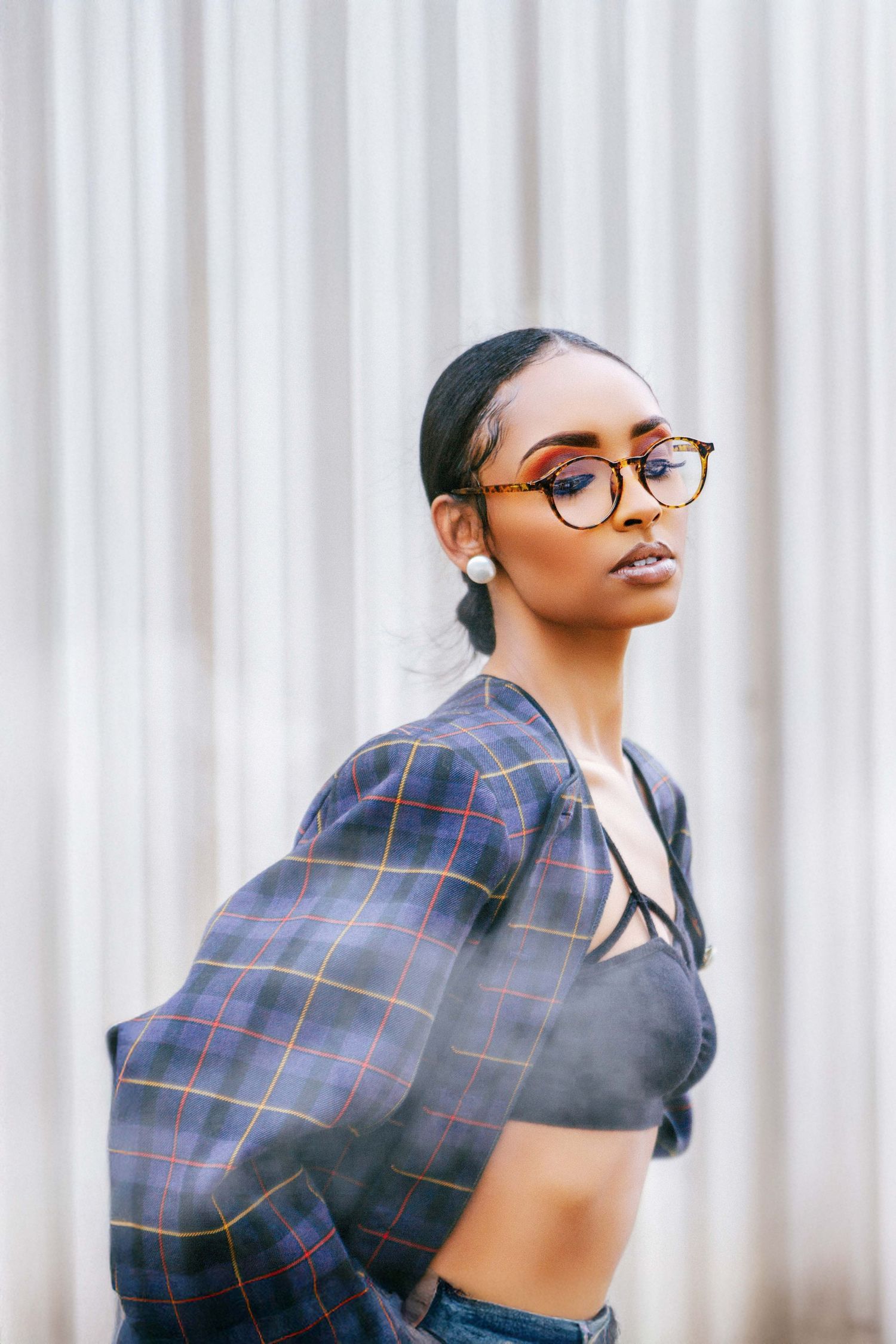 Stylish portrait featuring plaid jacket and glasses against white background.