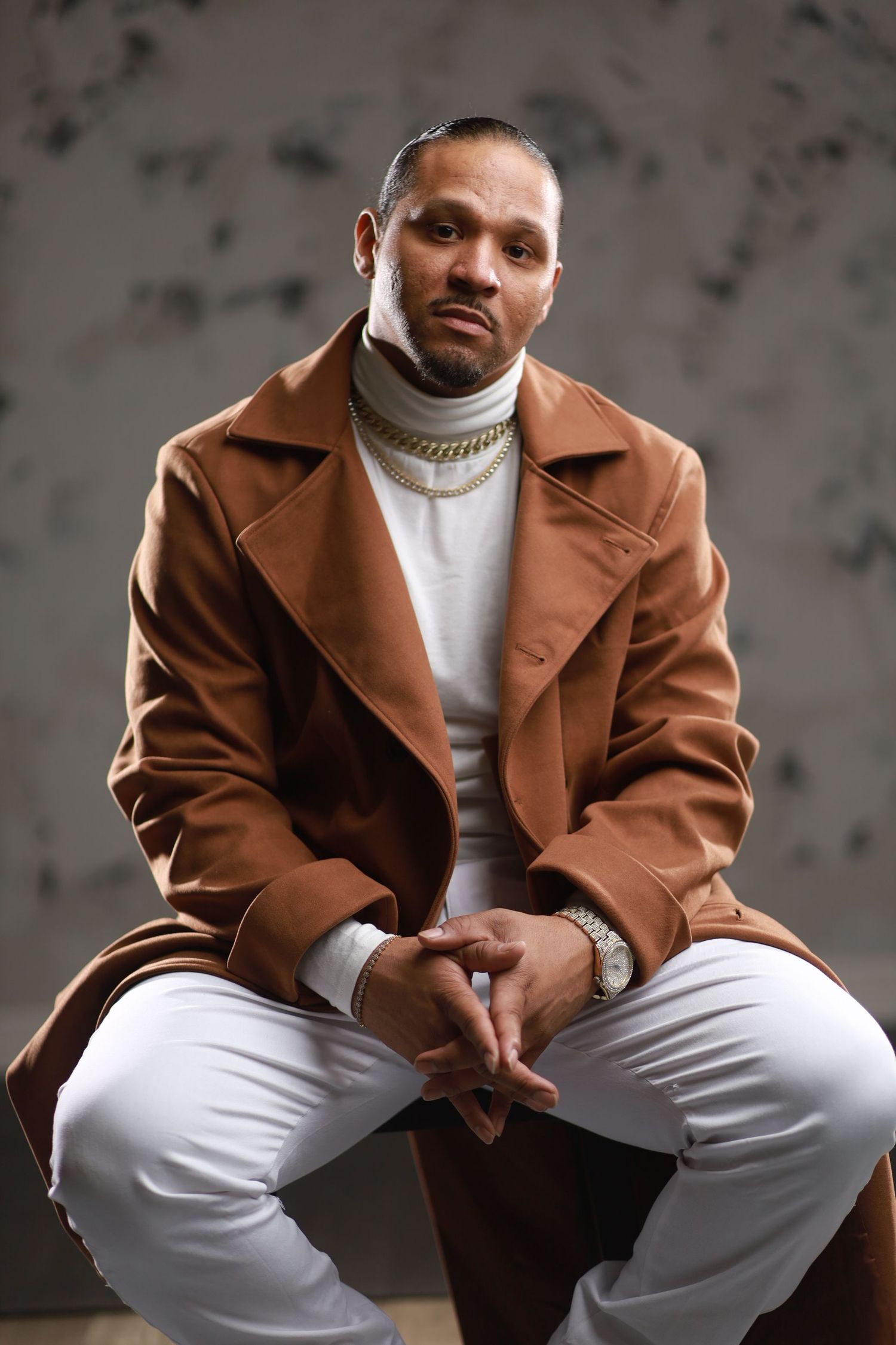 Professional portrait in brown coat and white turtleneck against textured background.