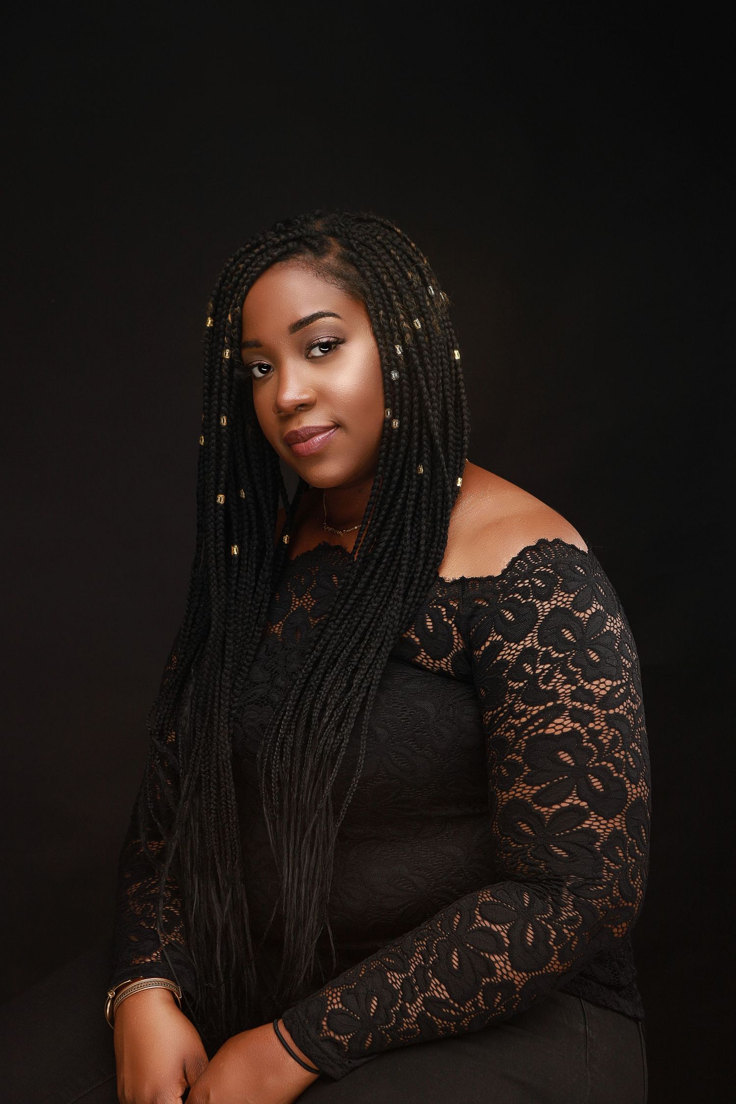 Elegant portrait in black lace dress with long braided hair adorned with gold accessories.
