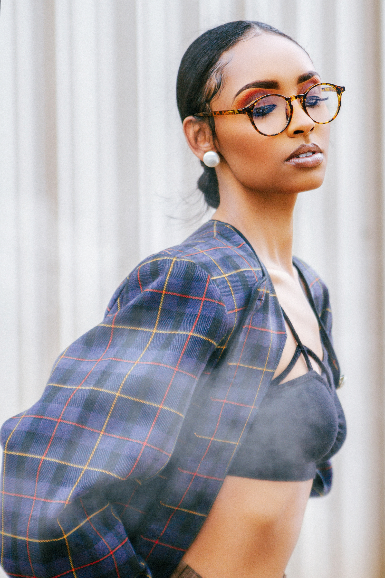 Portrait of fashionable person in plaid jacket and glasses against white striped wall.