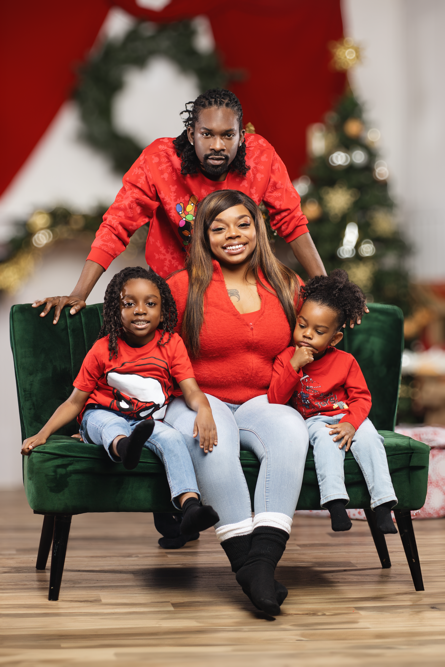 Festive family holiday portrait on green velvet chair with Christmas decorations in background.
