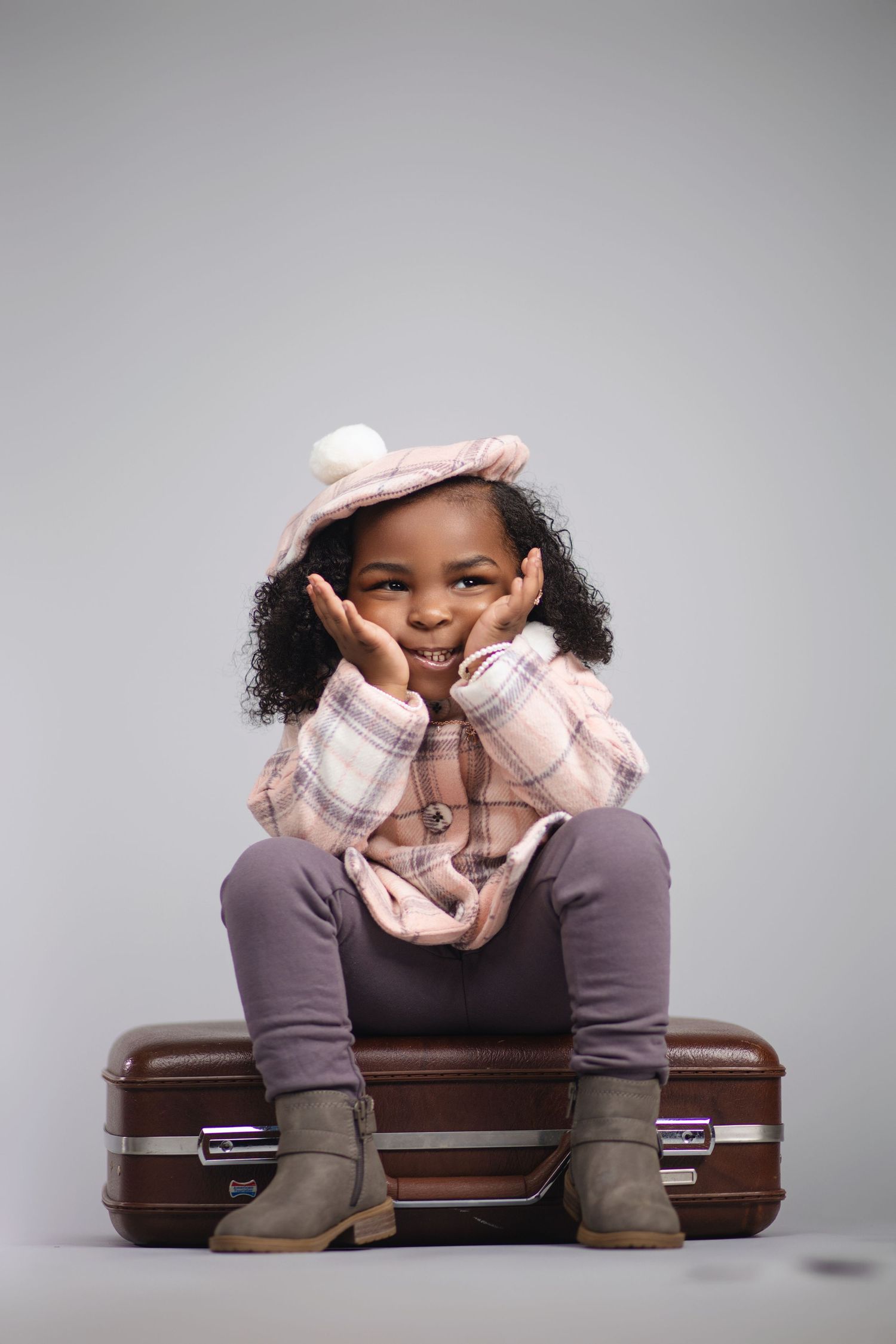 Charming portrait of a child in winter clothing sitting on vintage luggage.