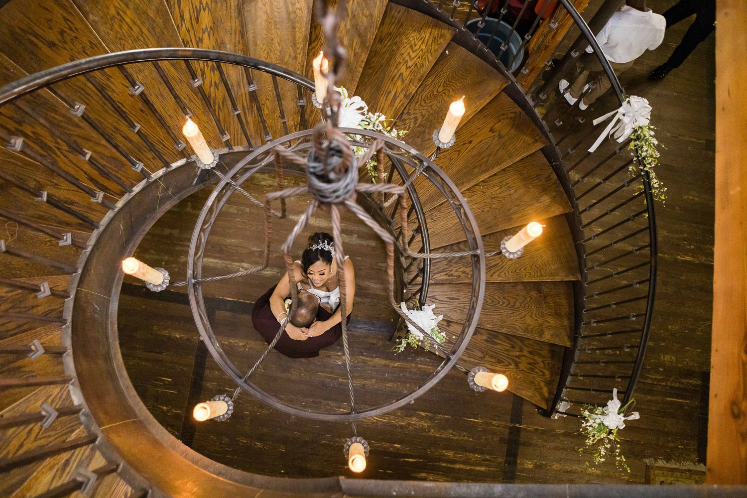 Artistic overhead view of spiral staircase with hanging lights and floral decorations.