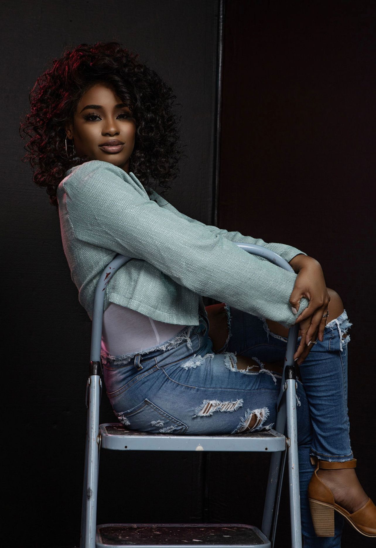 Stylish casual portrait on metal step ladder wearing denim and gray sweater.