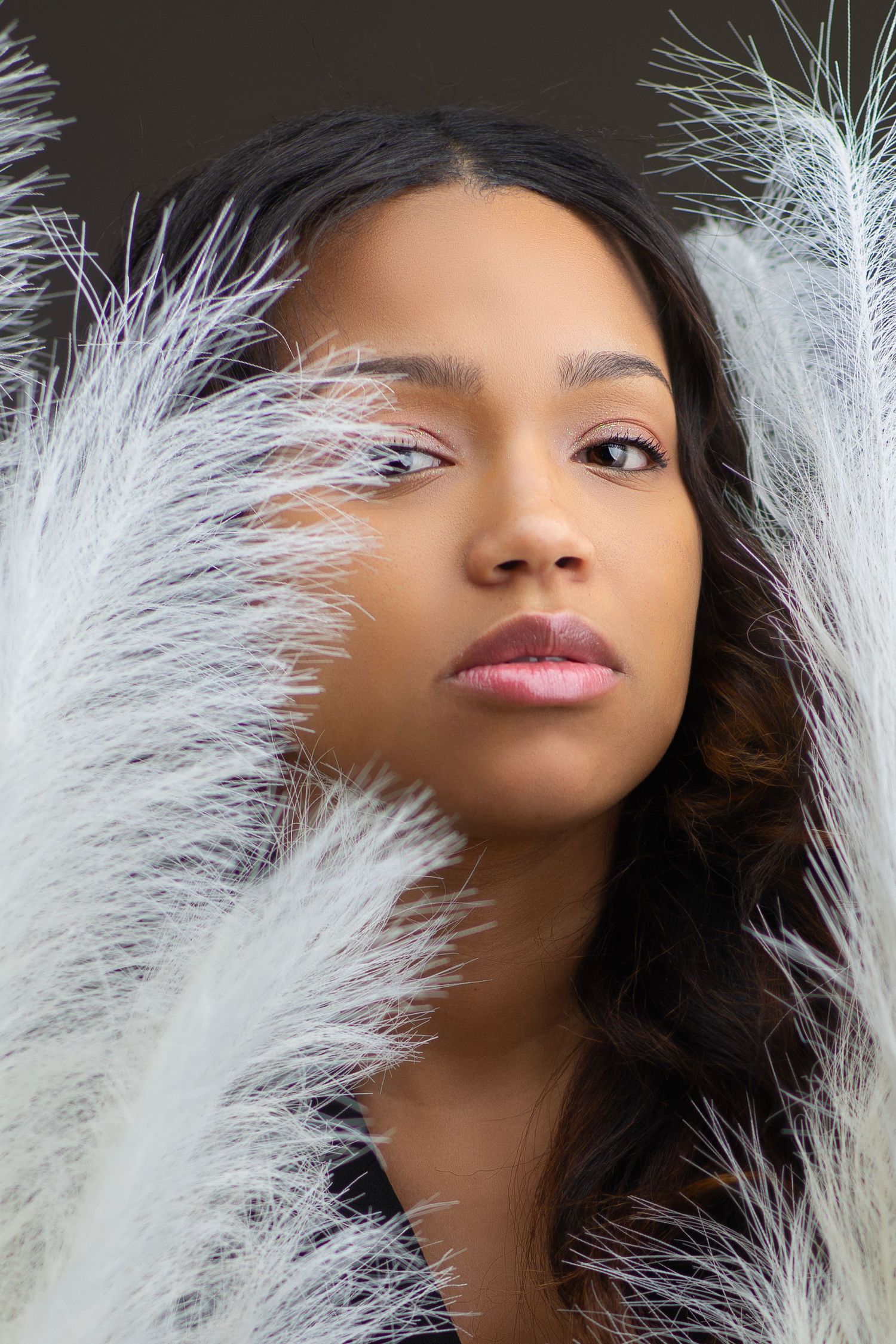 Beauty portrait with white feathers framing the face in soft lighting.
