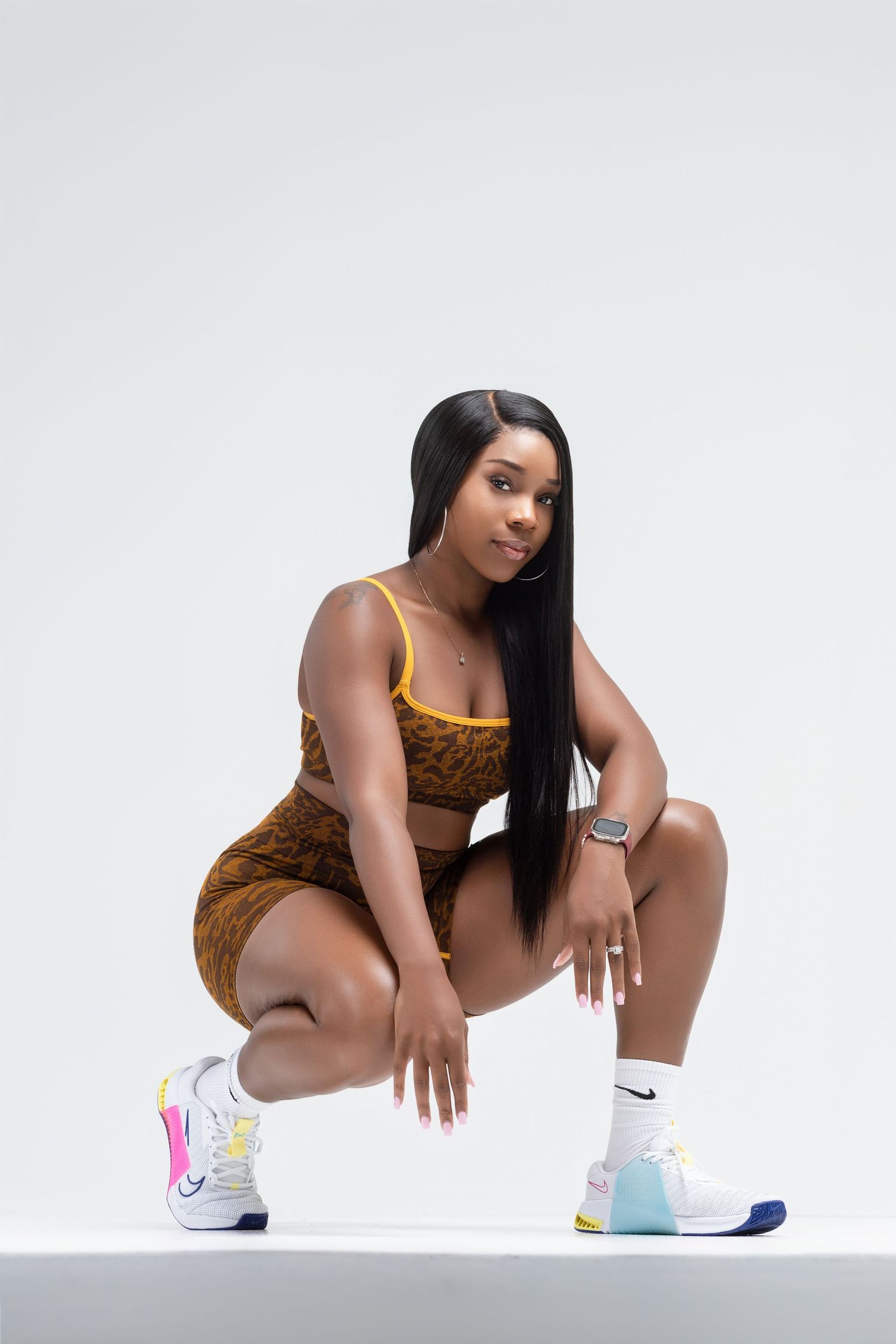 Athletic fashion photo of someone in a brown bodysuit and Nike sneakers posing on white backdrop.