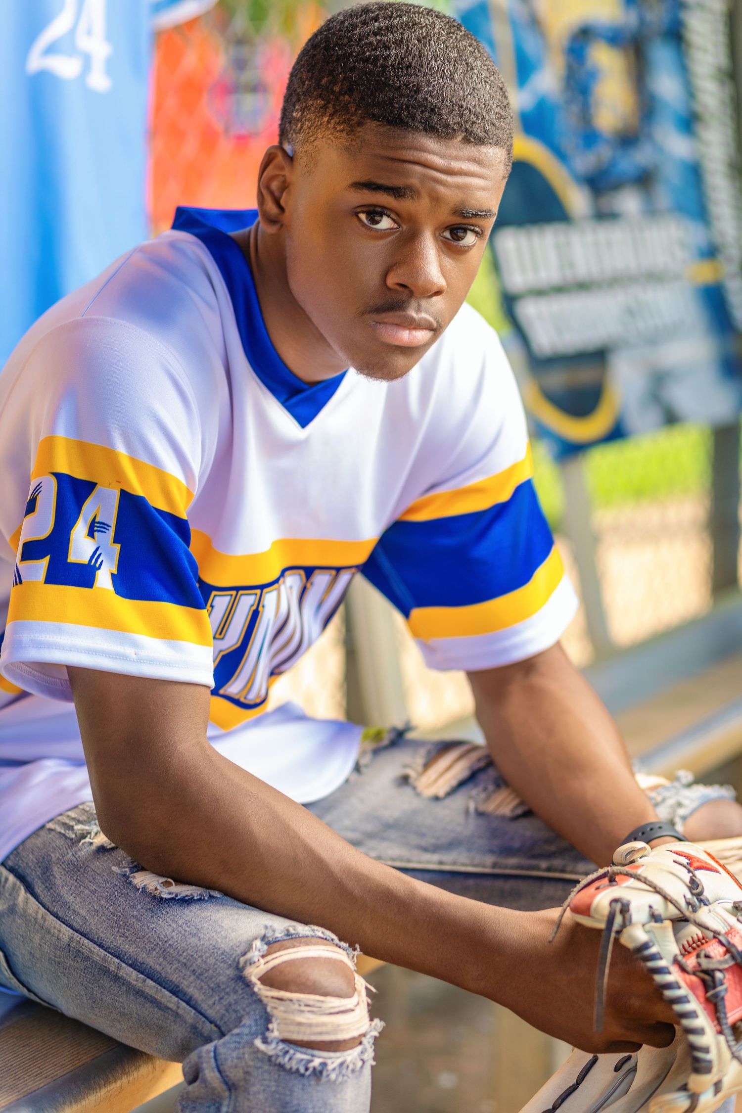 Baseball player in white and blue jersey sitting in dugout.