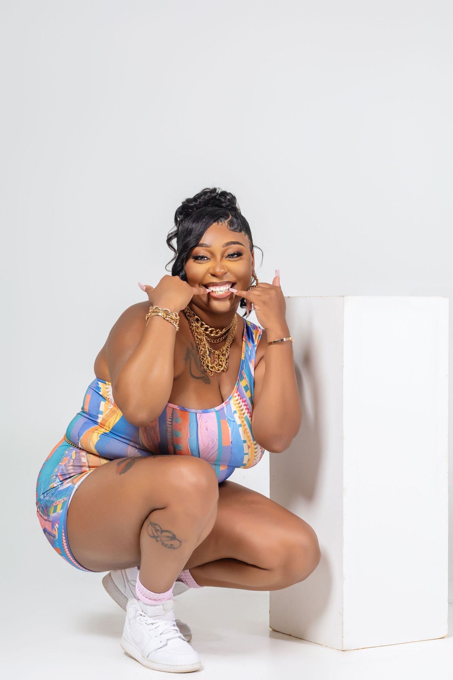 Fashion portrait of someone in a colorful striped romper and white sneakers against a white backdrop.