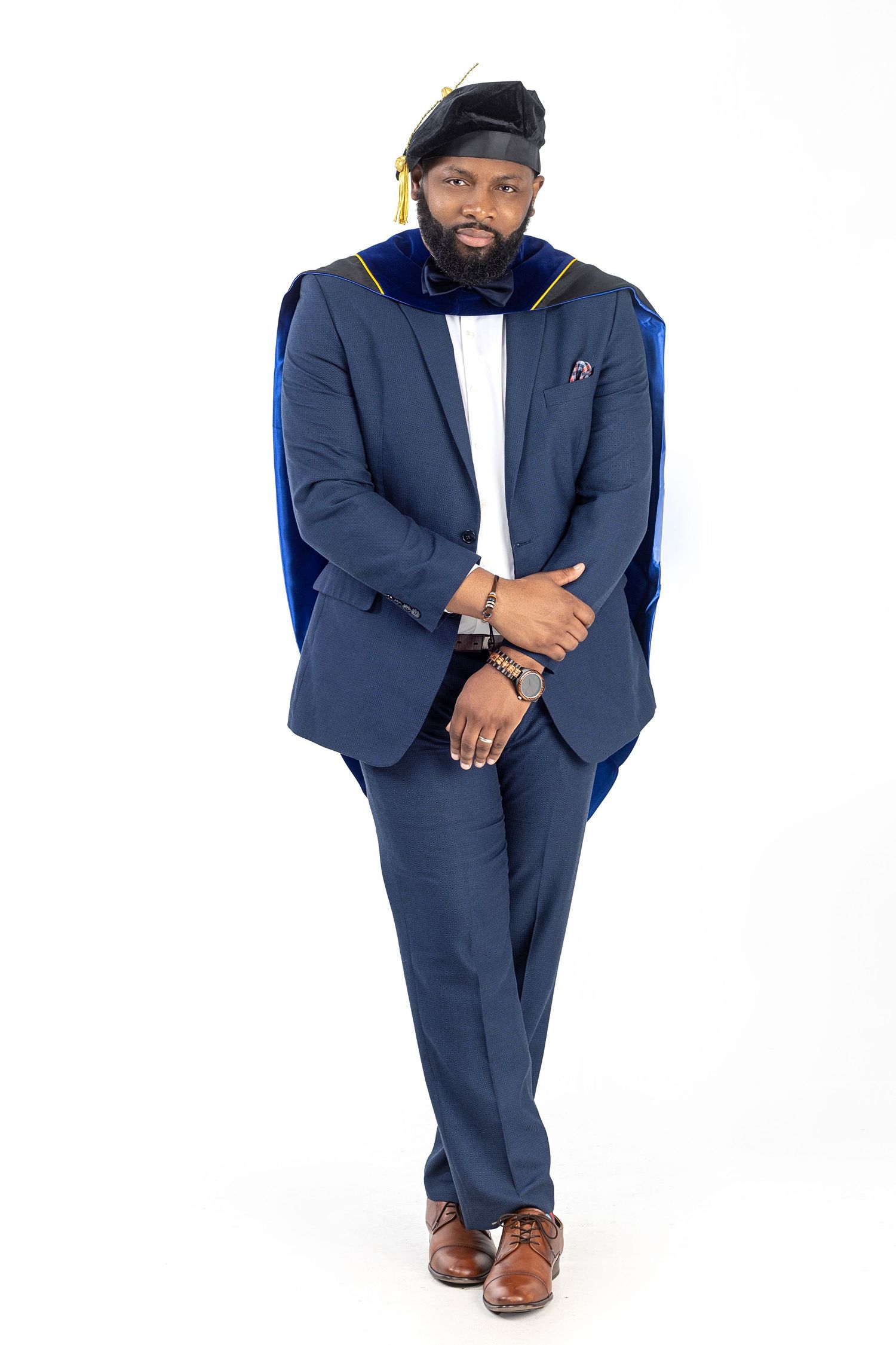 Professional man in navy suit and cap poses confidently against white background.