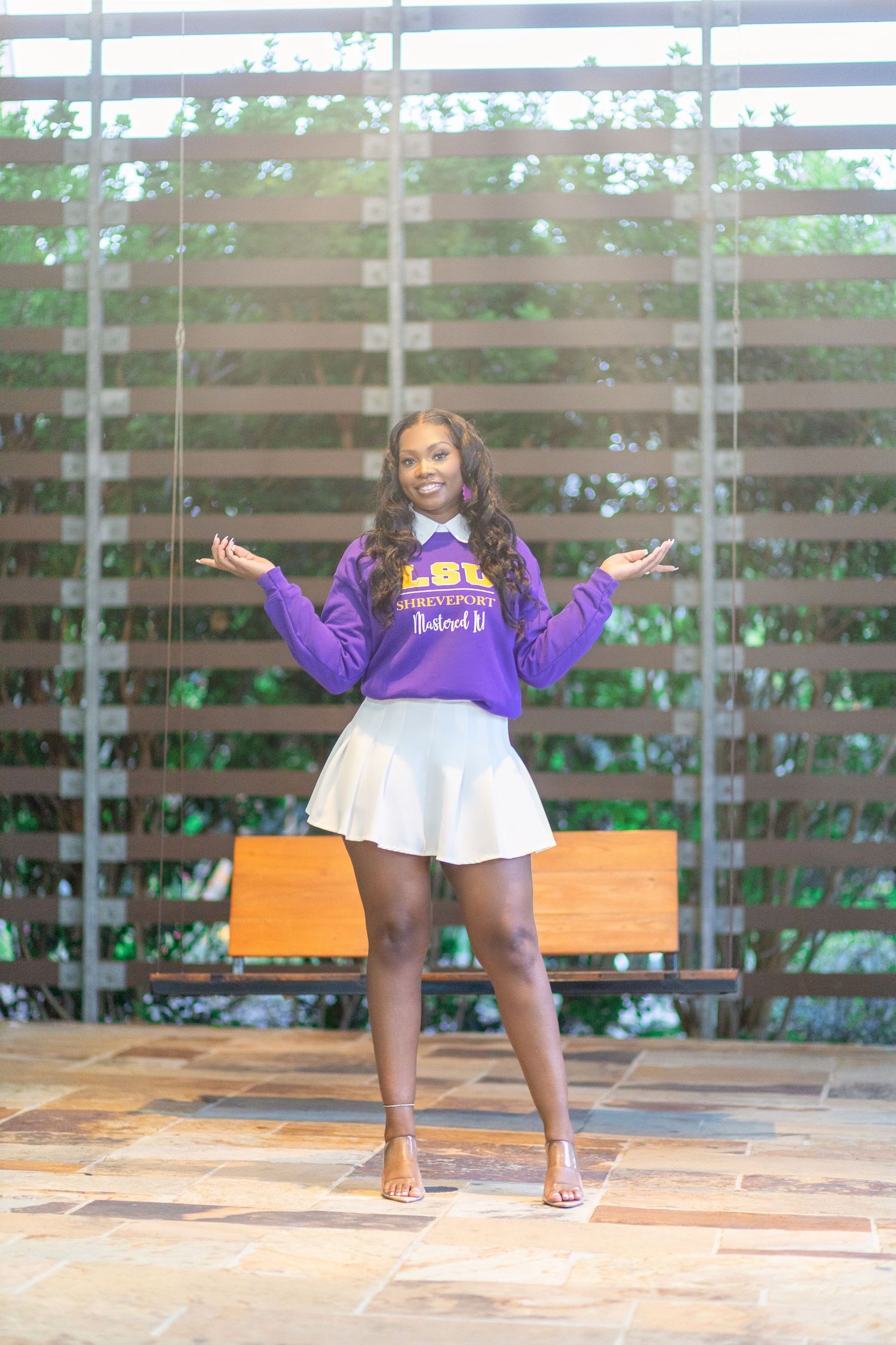 Casual pose in purple sweater and white skirt against modern architectural backdrop.