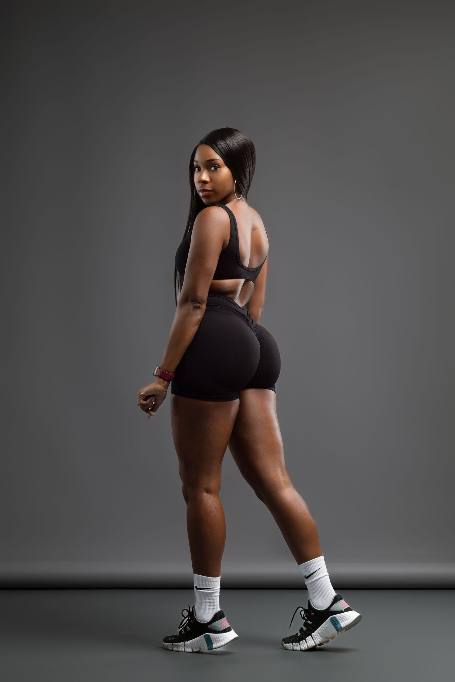 Athletic figure in black workout attire and sneakers poses against dark background.