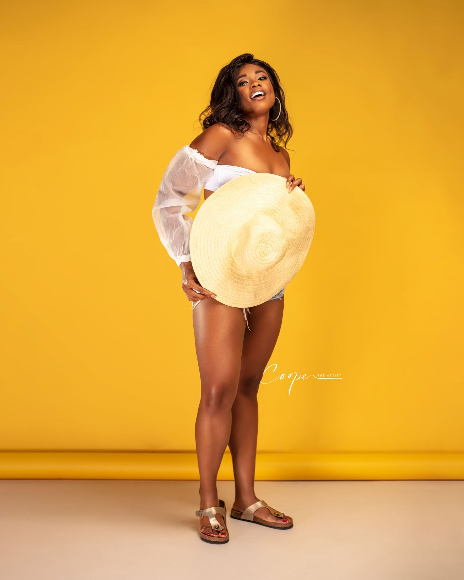 Playful summer portrait against yellow background with white top and straw hat.