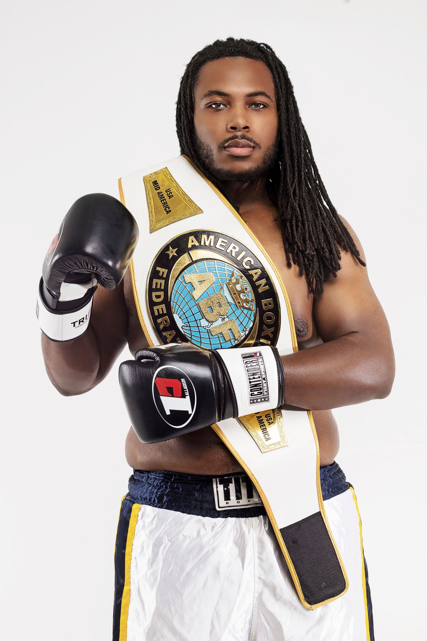 Athletic boxer poses with championship belt and boxing gloves against white background.