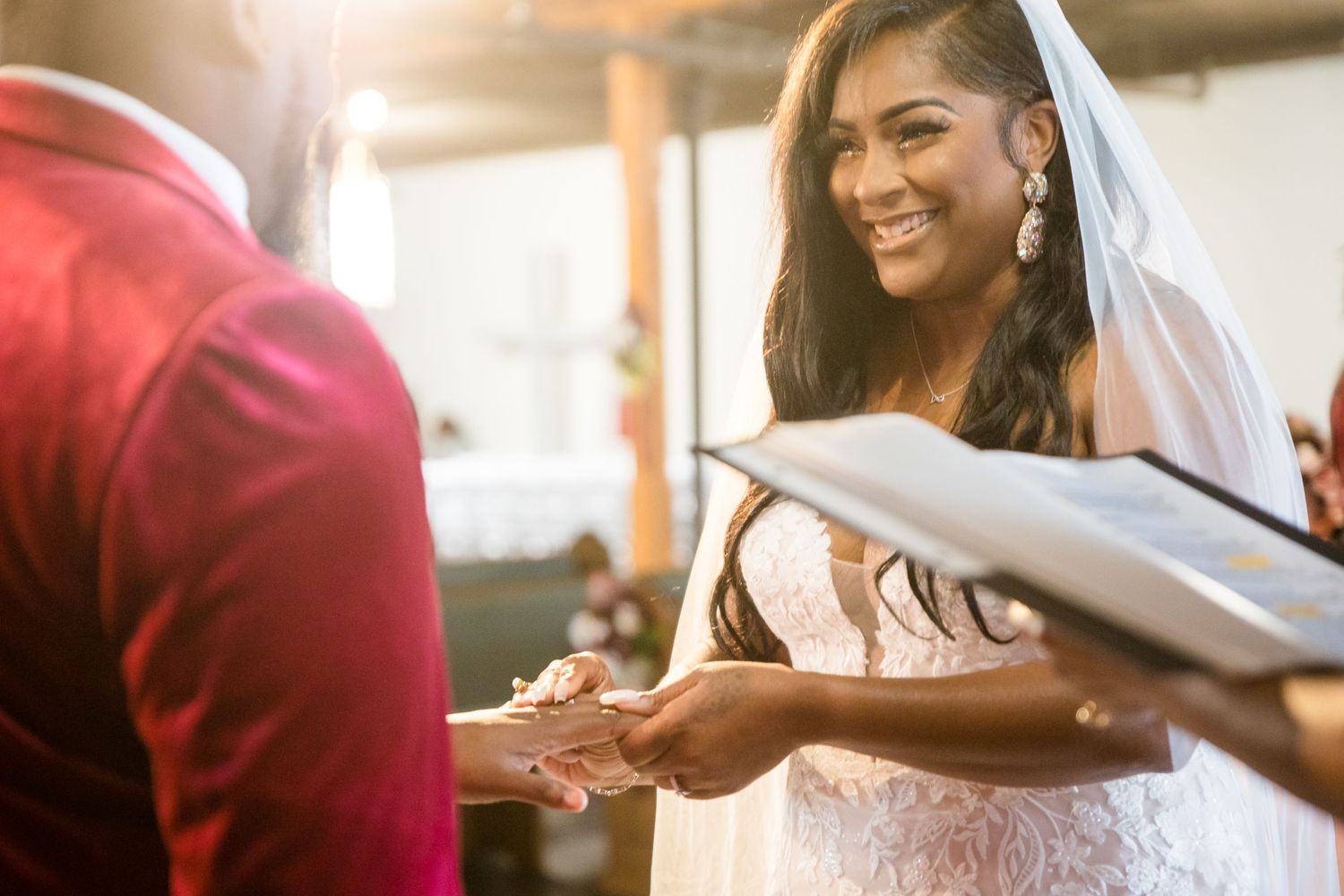 A joyful bride in a white dress smiles while reviewing paperwork during what appears to be a wedding ceremony.