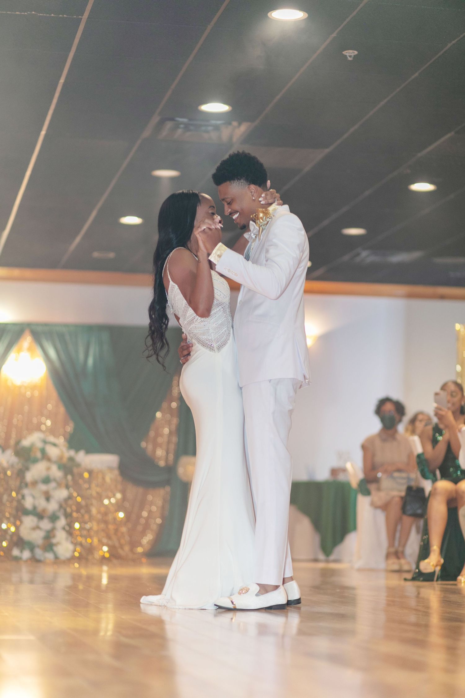 Newlywed couple sharing their first dance in white attire at wedding reception.