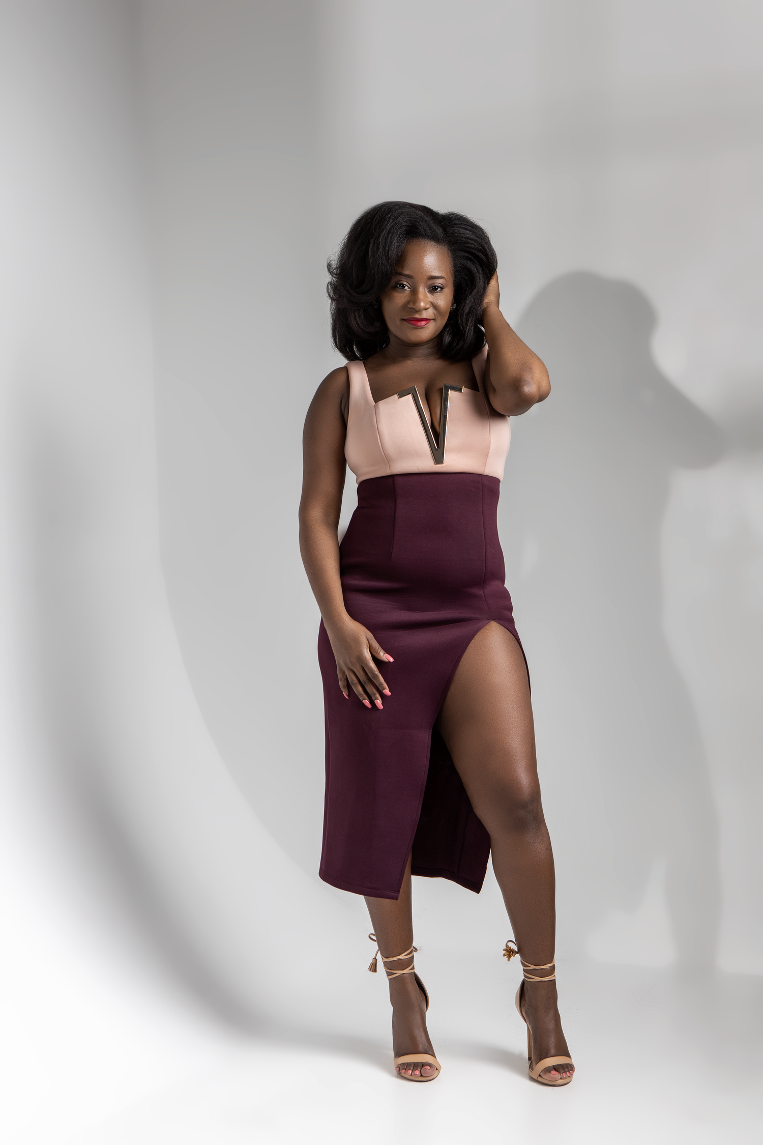 Fashion portrait in pink and burgundy dress with leg slit against white background.