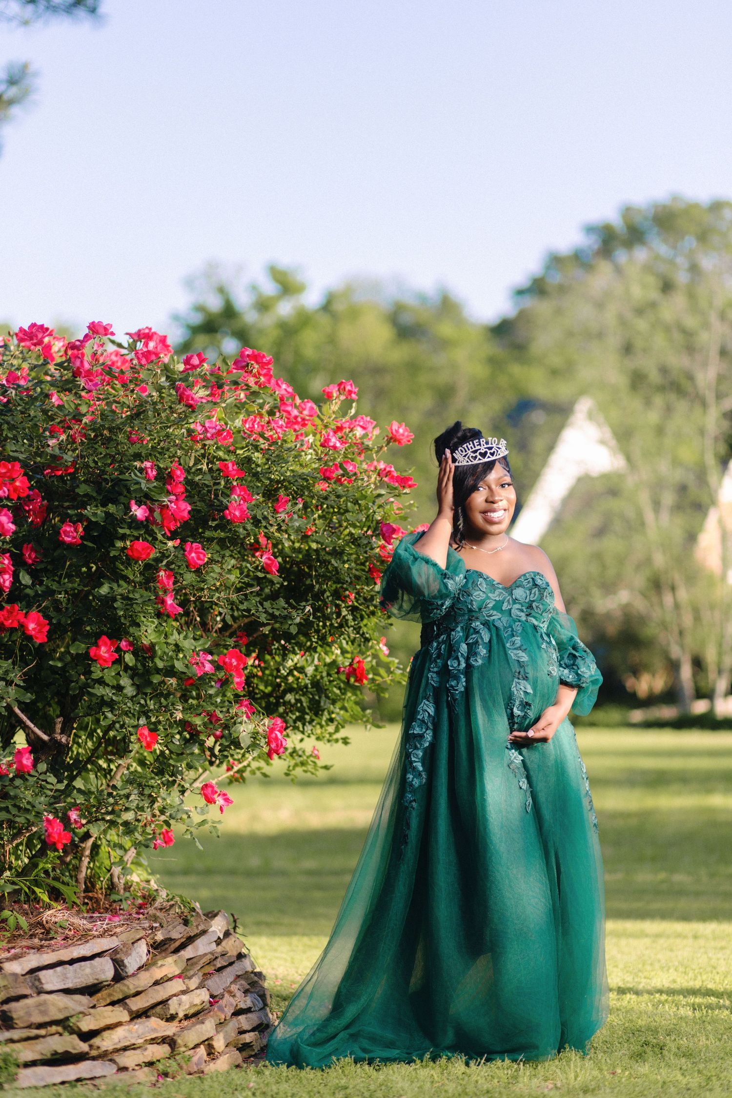 Outdoor portrait in emerald green gown beside blooming pink rose bush.