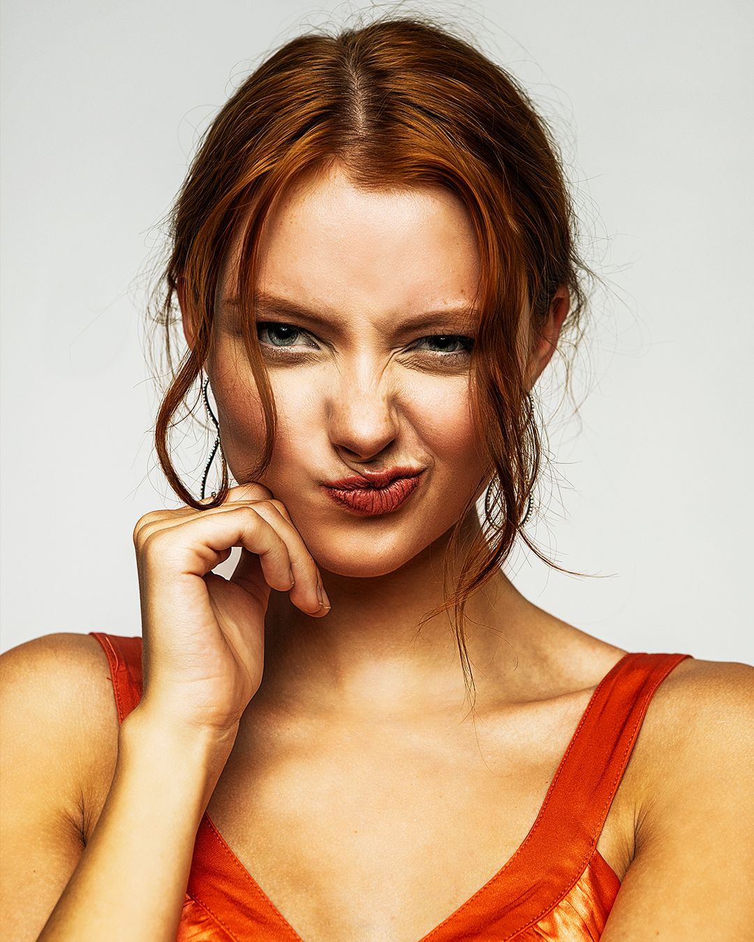 Beauty portrait with red top and upswept hairstyle against light background.