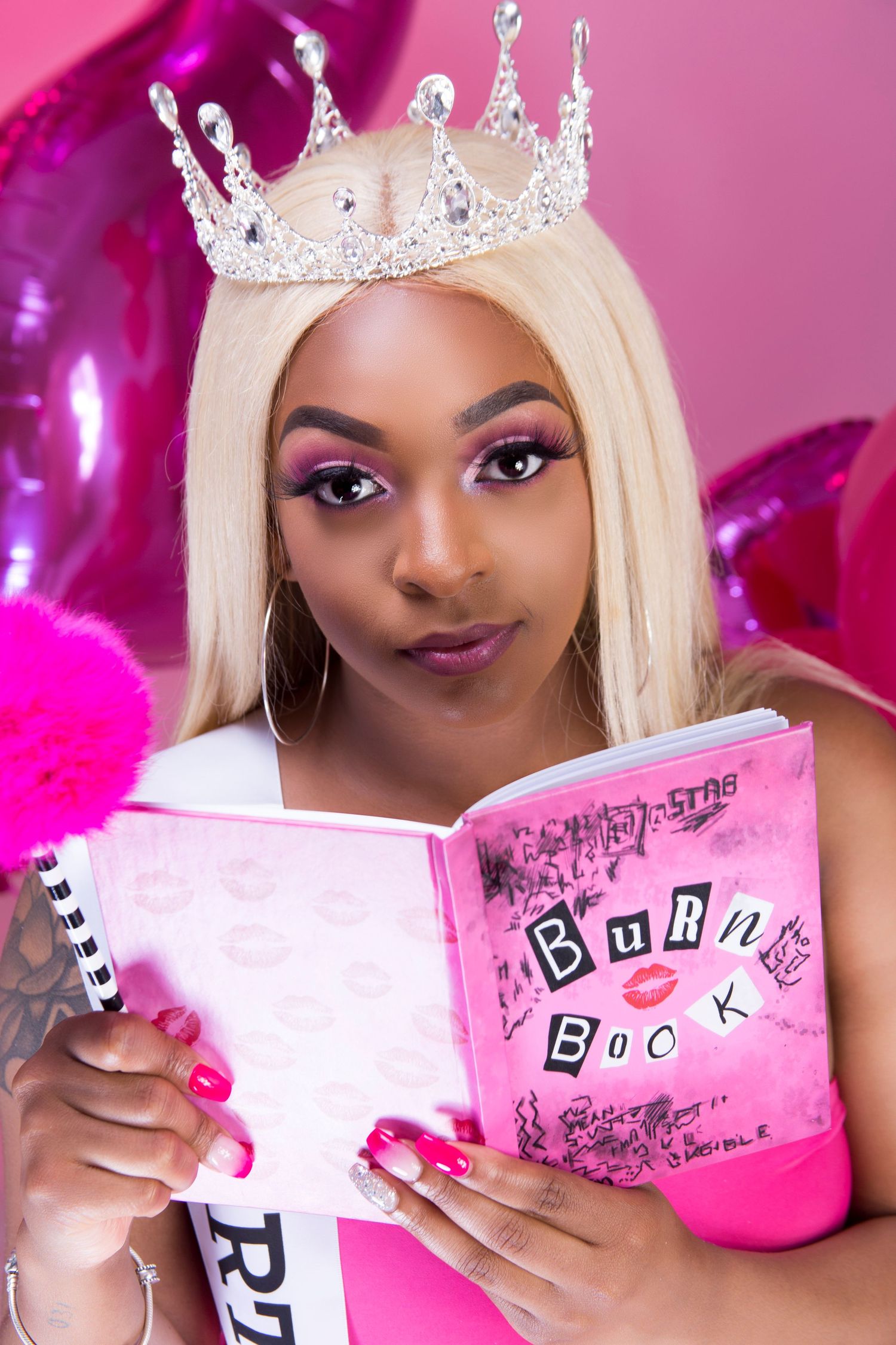 Whimsical portrait with tiara and pink book against pink balloon backdrop.