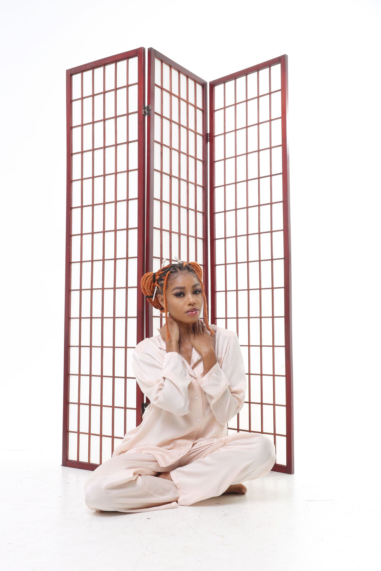 Portrait in soft pajamas posed against red room divider screen.