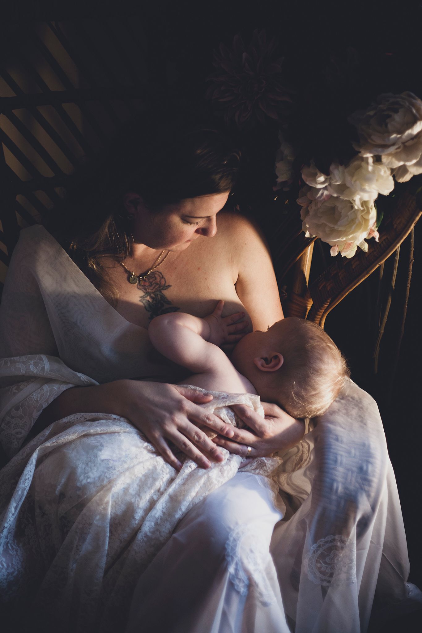 Porträtt på en mamma som amar sin son, i en vacker rottingfotölj med blommor, mörkare ljussättning, konstnärligt porträtt.