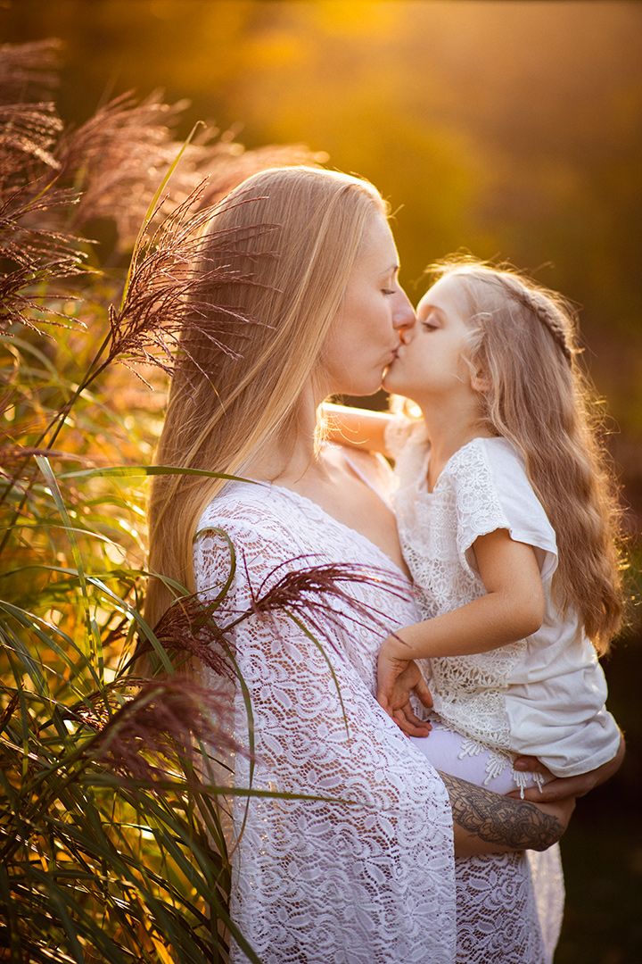 Vackert porträtt på en mamma och sin dotter som står bland högt pampas gräs i solnedgången. Vota spetskläder, varmt ljus, naturliga färger.