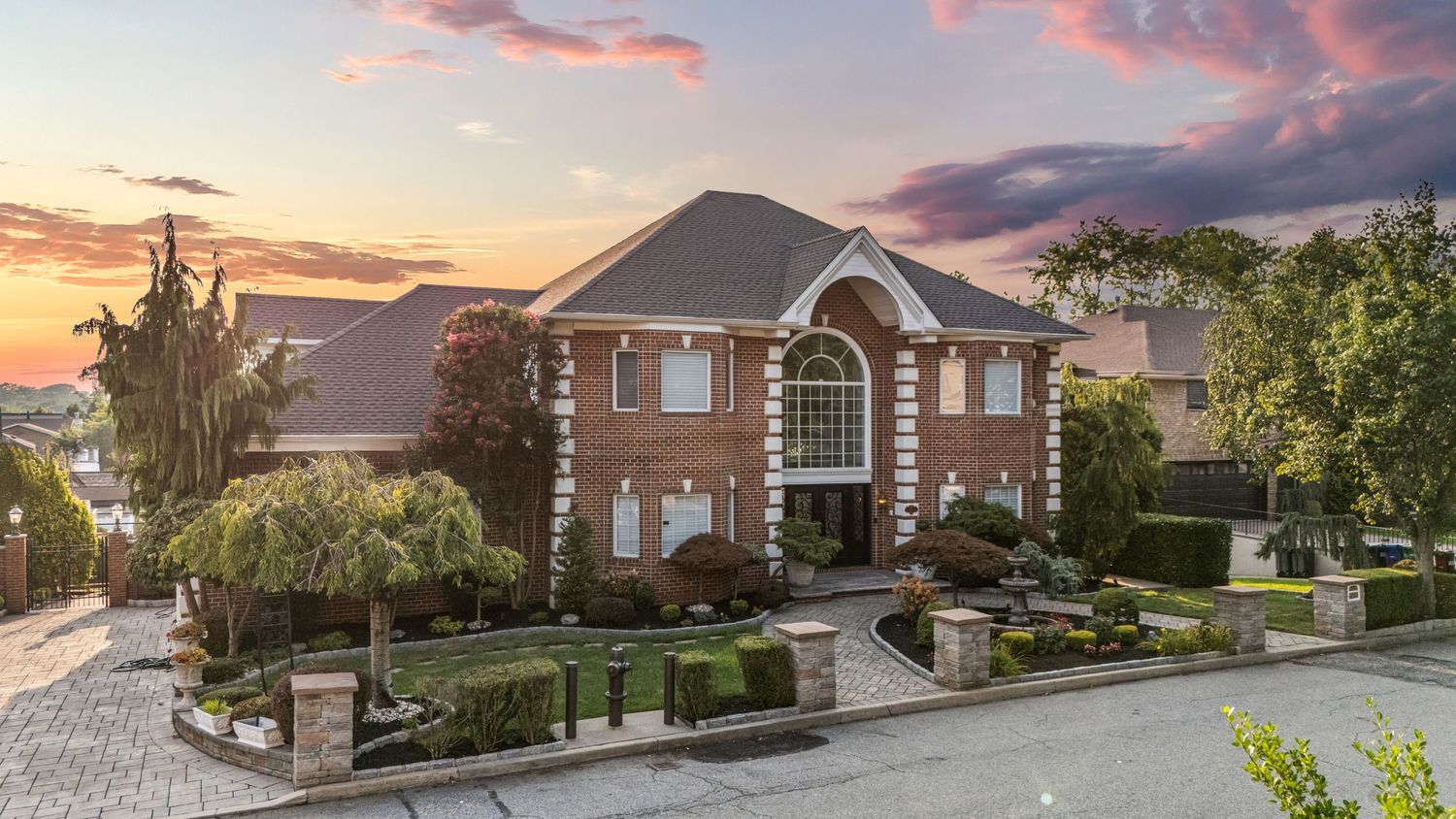 Panoramic view of luxury estate entrance with stone pillars during colorful sunset.