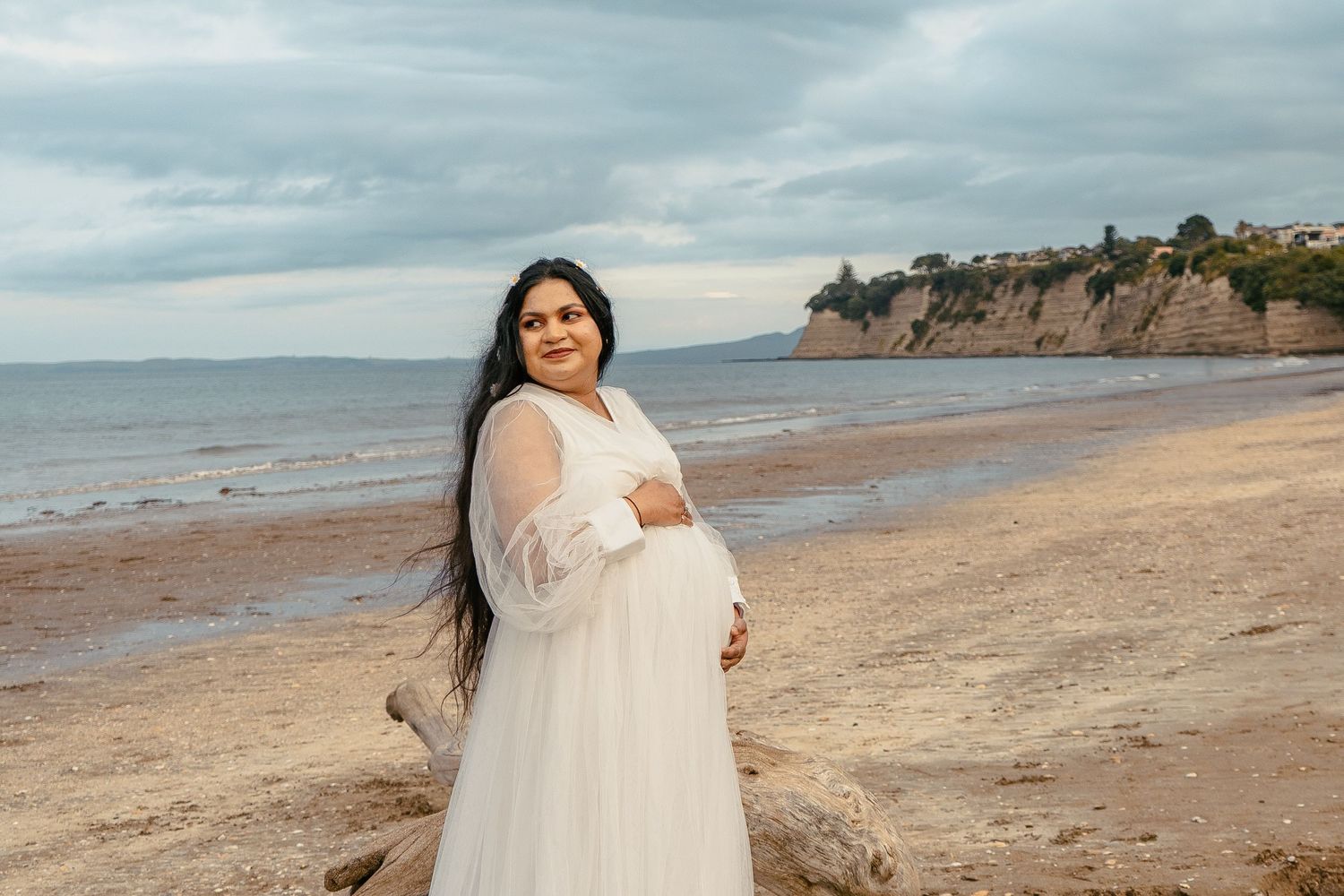 A gorgeous maternity shoot during sunset at Long Bay Beach, Auckland by YM Photography. White, flowy maternity dress used from Shein.